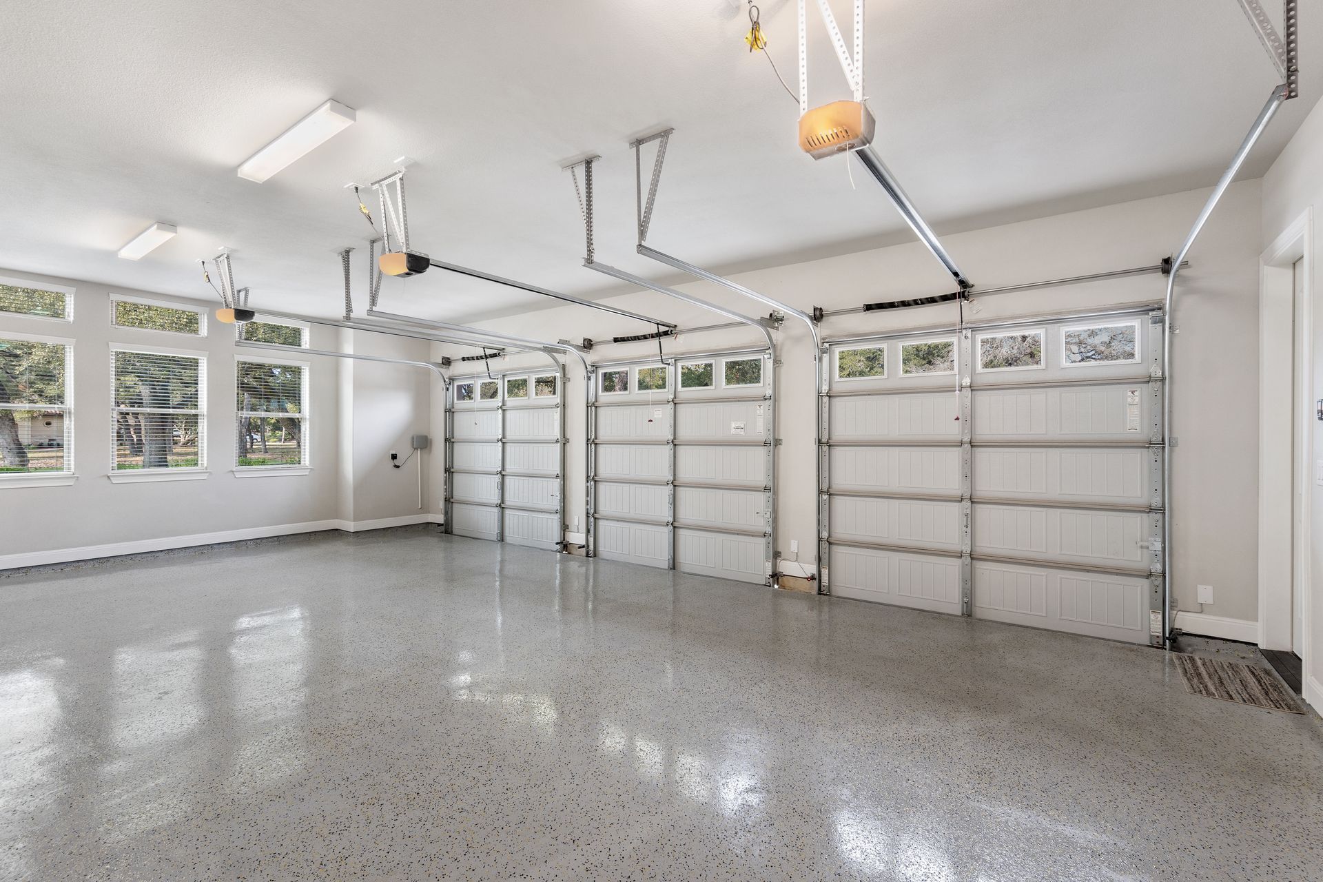 Empty white garage with three doors, windows, and a speckled concrete floor