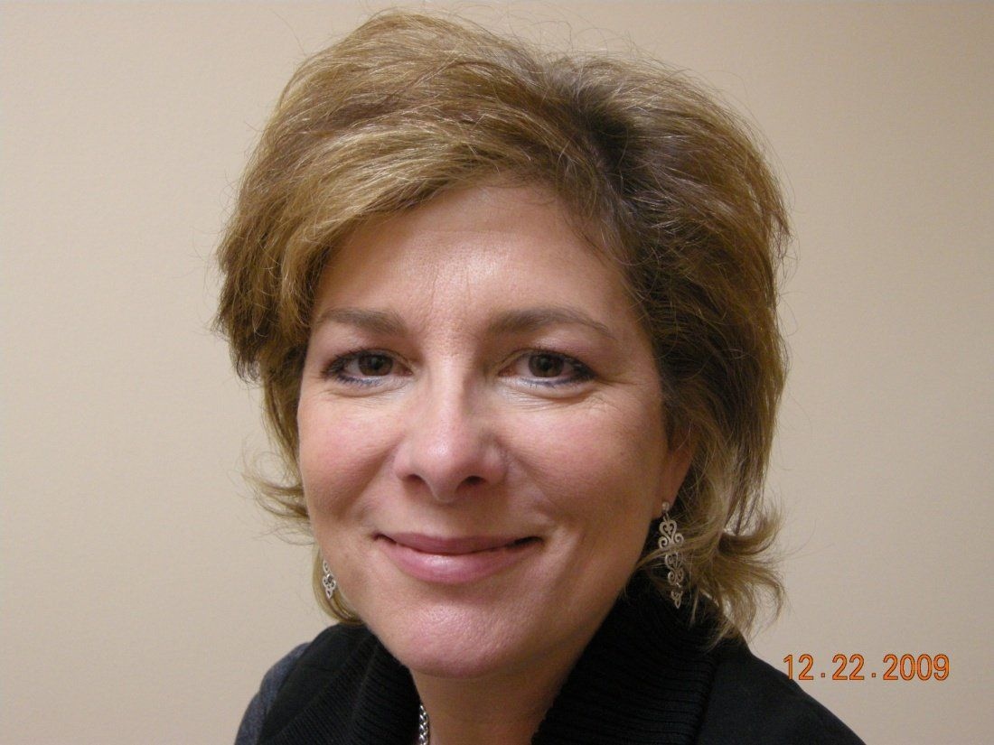 Woman with short, light brown hair, smiling, in front of a neutral-colored wall.