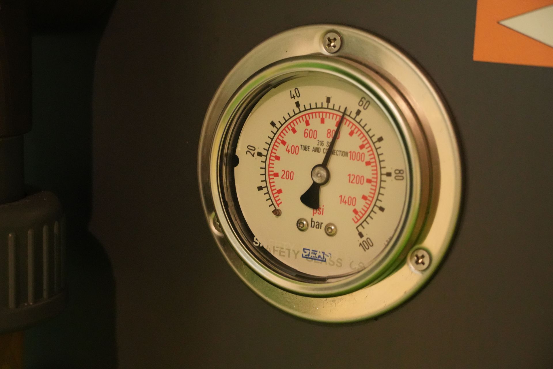 A close-up of a precise industrial pressure gauge displaying readings in bars and PSI on a machine.