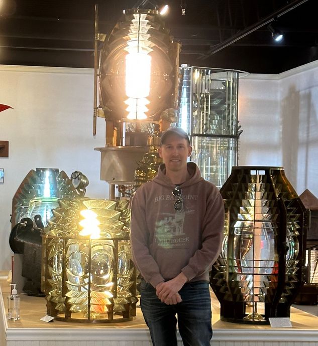 A man in a hoodie is standing in front of a lighthouse