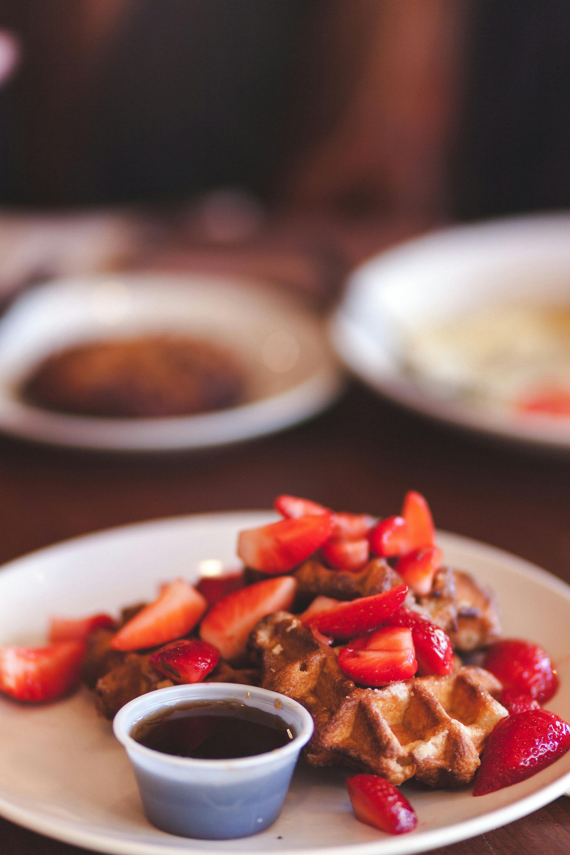 A plate of waffles with strawberries and syrup on a table.