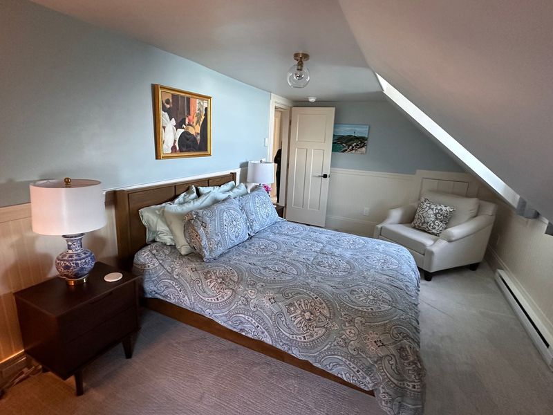 A peaceful bedroom with a large bed, warm lighting, and a painting hanging over the bed.