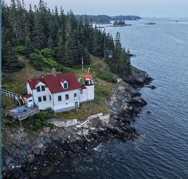 A lighthouse is sitting on top of a grassy hill next to a body of water.