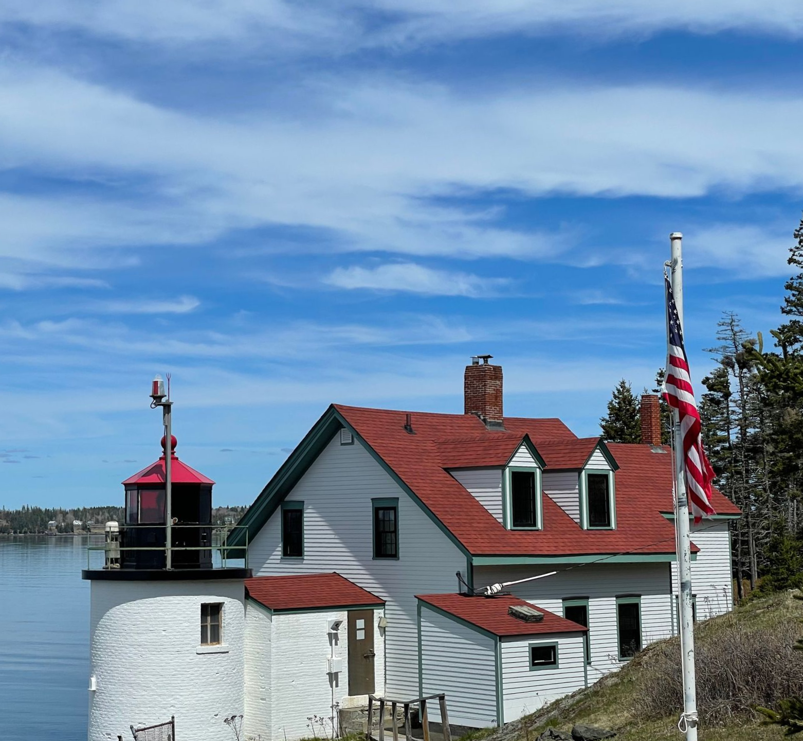 A white house with a lighthouse on top of it next to a body of water.