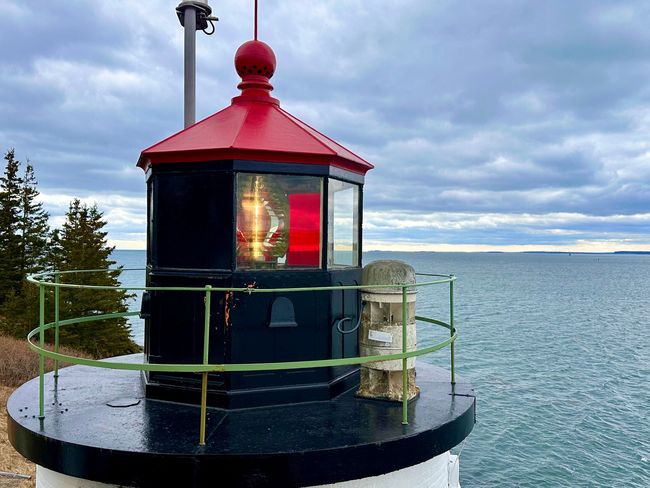 Small red-topped lighthouse on a rocky shore with a cloudy sea backdrop