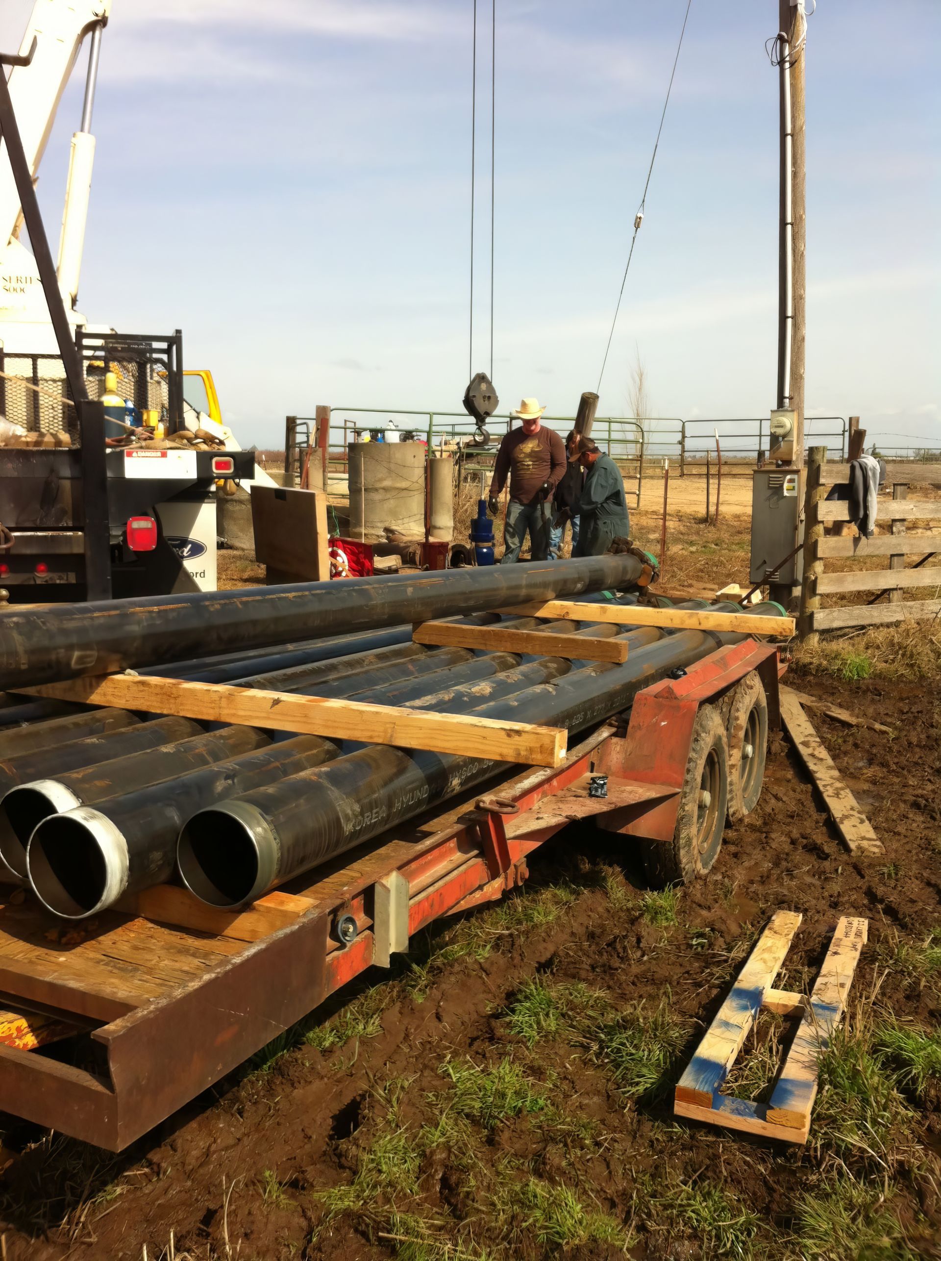 Construction site with stacked metal pipes on a trailer and workers in the background under a clear sky