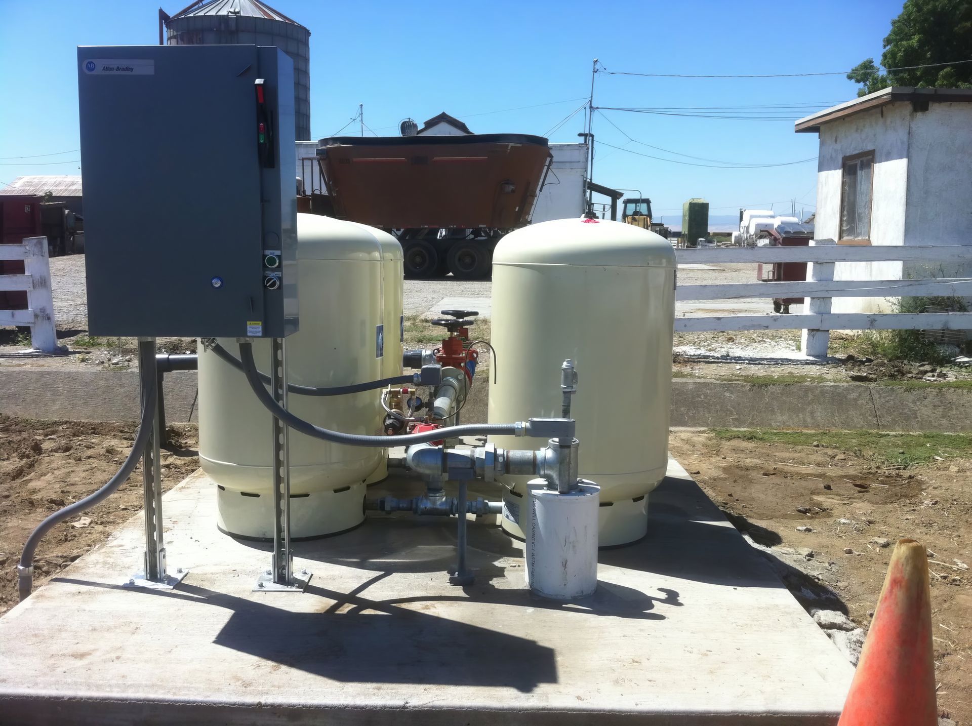 Industrial equipment with two beige tanks and a blue control box on a concrete pad outdoors.