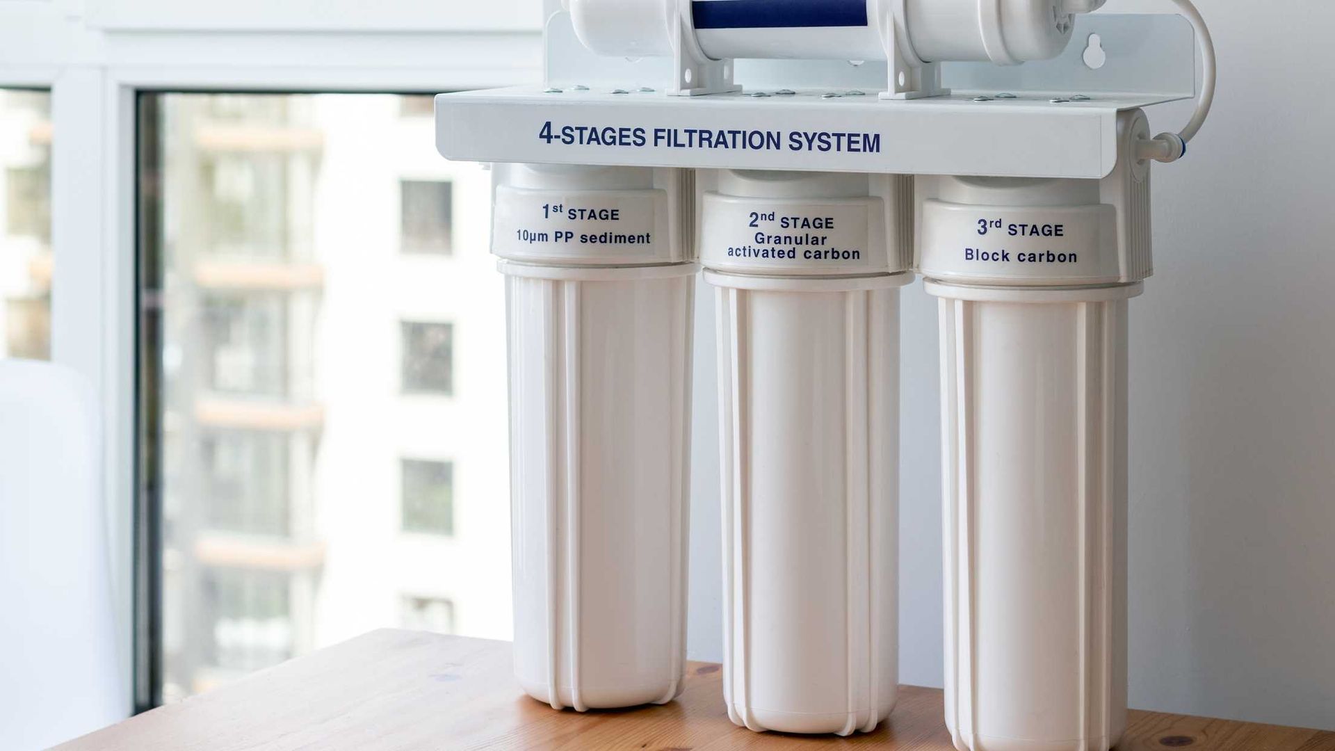 White 4-stage water filtration system with three canisters on a countertop near a window