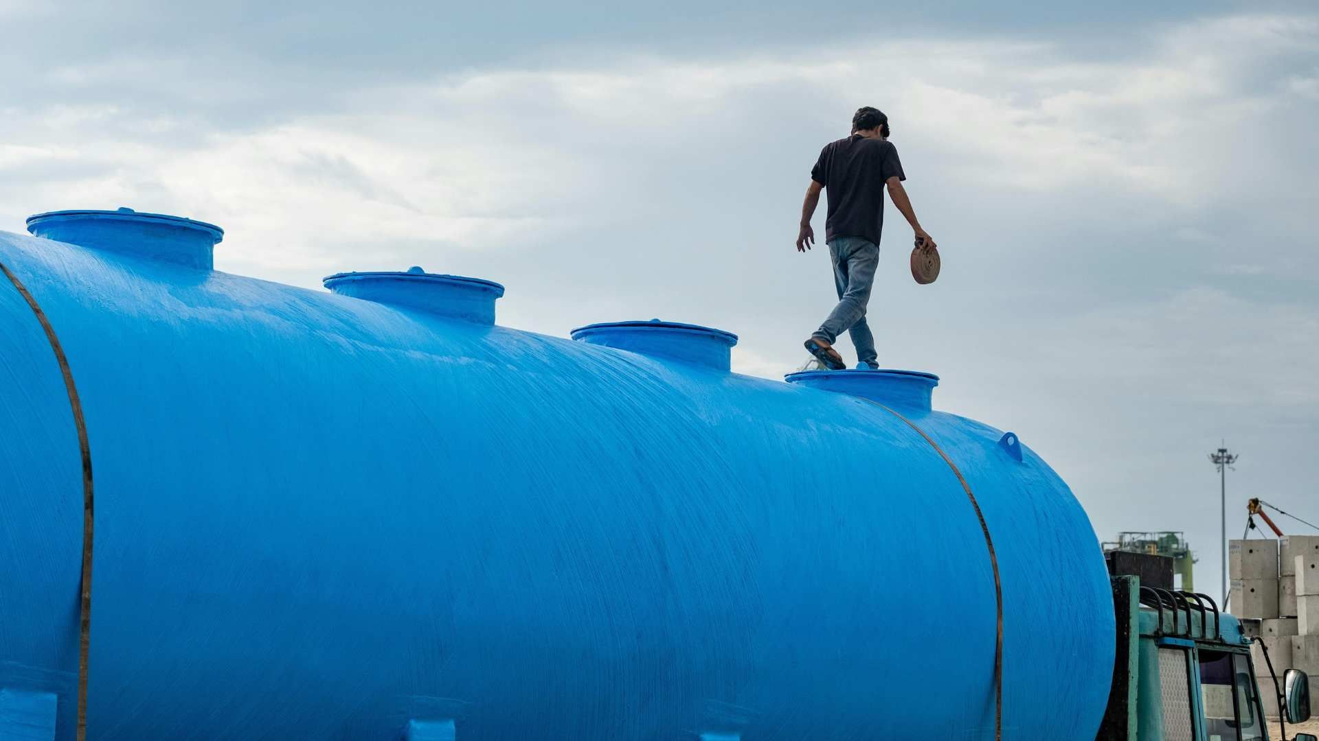 Worker standing on top of a large blue cylindrical tank under a cloudy sky