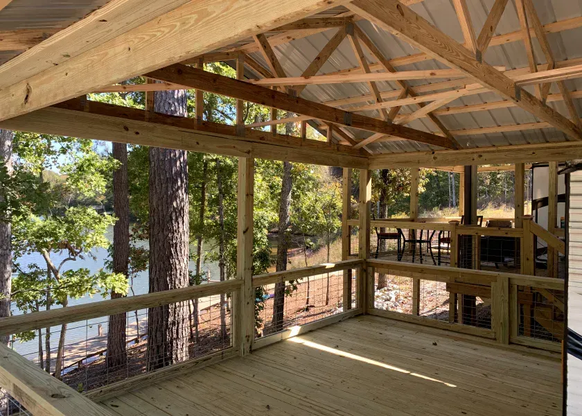 Wooden porch under construction with exposed beams, overlooking trees and a lake