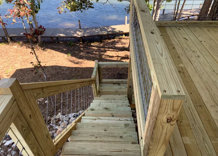 Wooden stairs descending to a lakeside deck, with water and shoreline trees beyond.