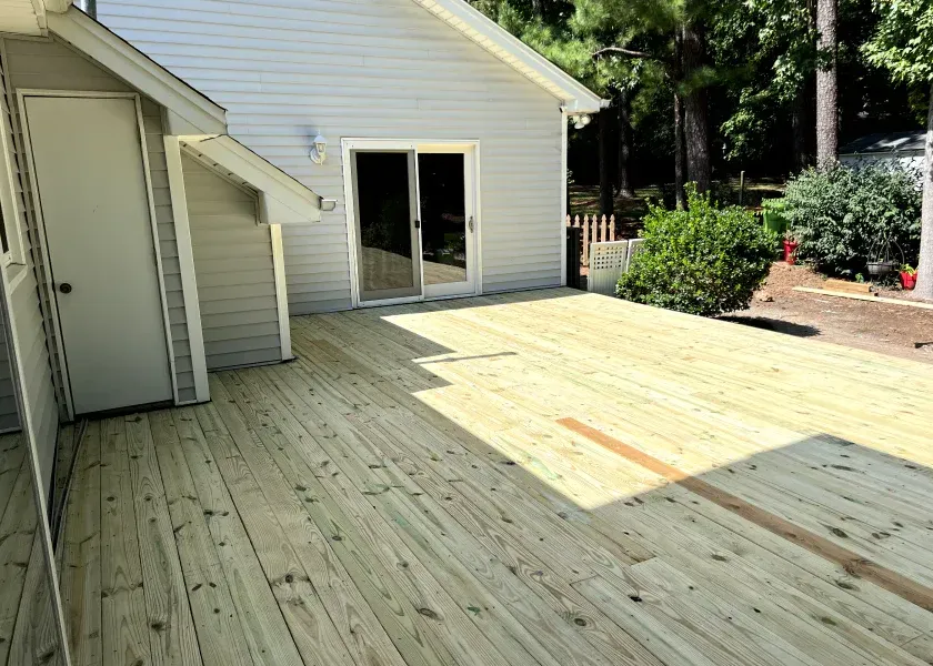 Freshly built wooden deck beside a light-sided house with sliding glass doors and a shaded yard