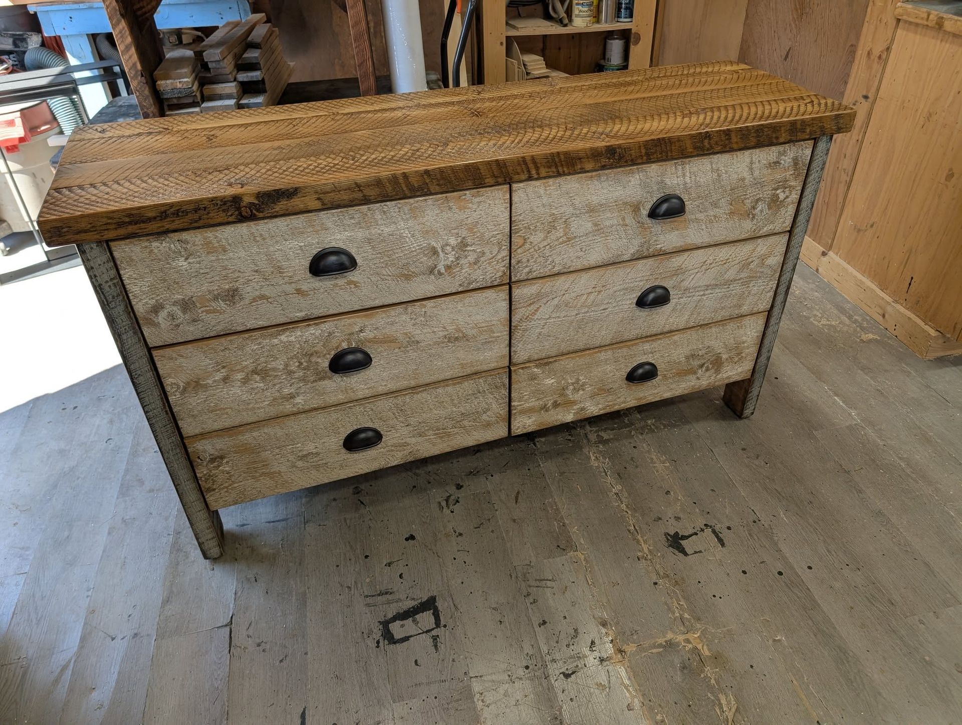 Rustic six-drawer dresser with woven top and black pulls in a workshop setting