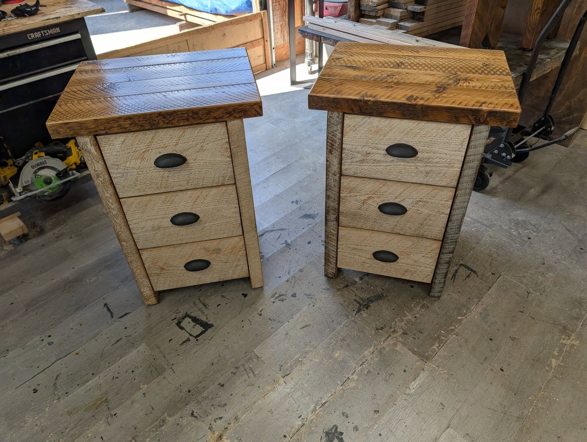 Two small rustic wooden three-drawer nightstands with speckled tops in a workshop