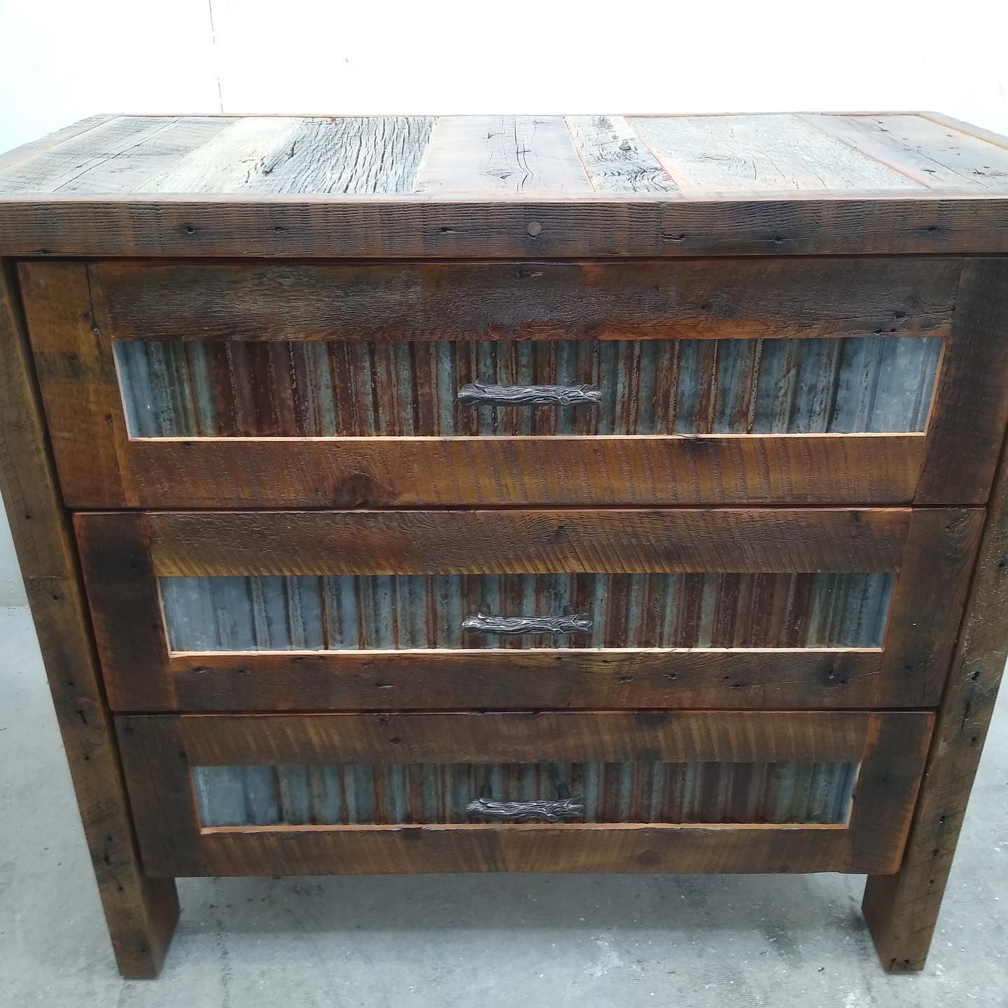Weathered wooden dresser with three drawers and corrugated metal panels on the front