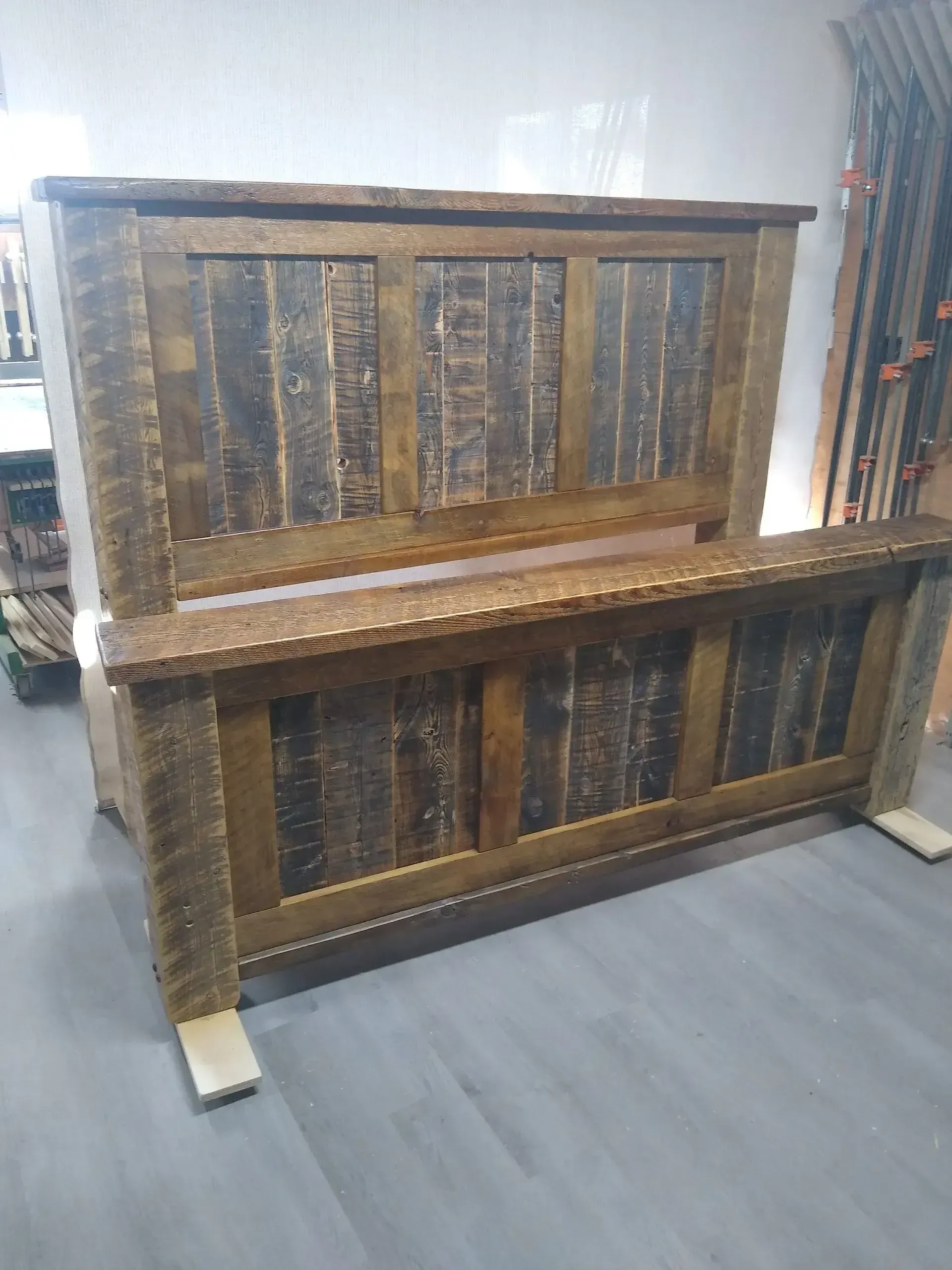 Two stacked wooden crates or pallets in a warehouse, with white plastic feet and a gray floor.