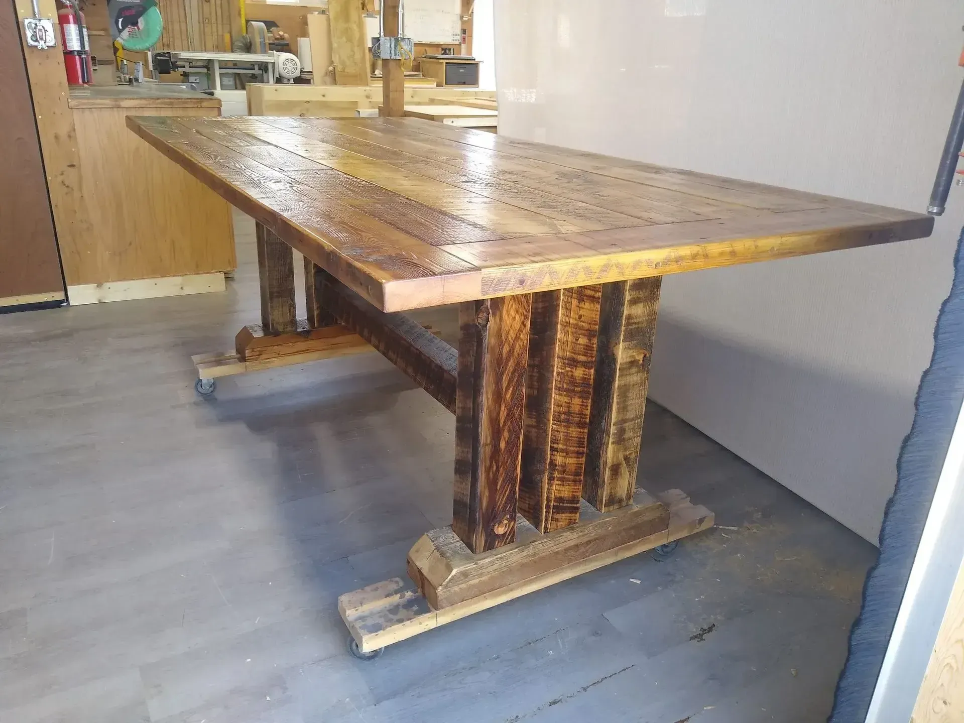 Rustic wooden table with a thick top and decorative base in a room with gray flooring.