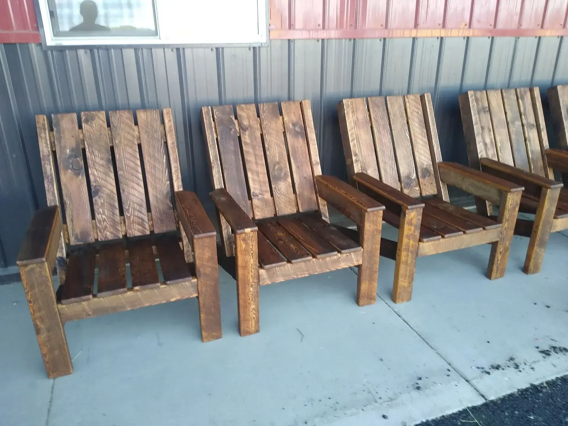 Row of weathered wooden chairs against a corrugated metal wall on a concrete floor