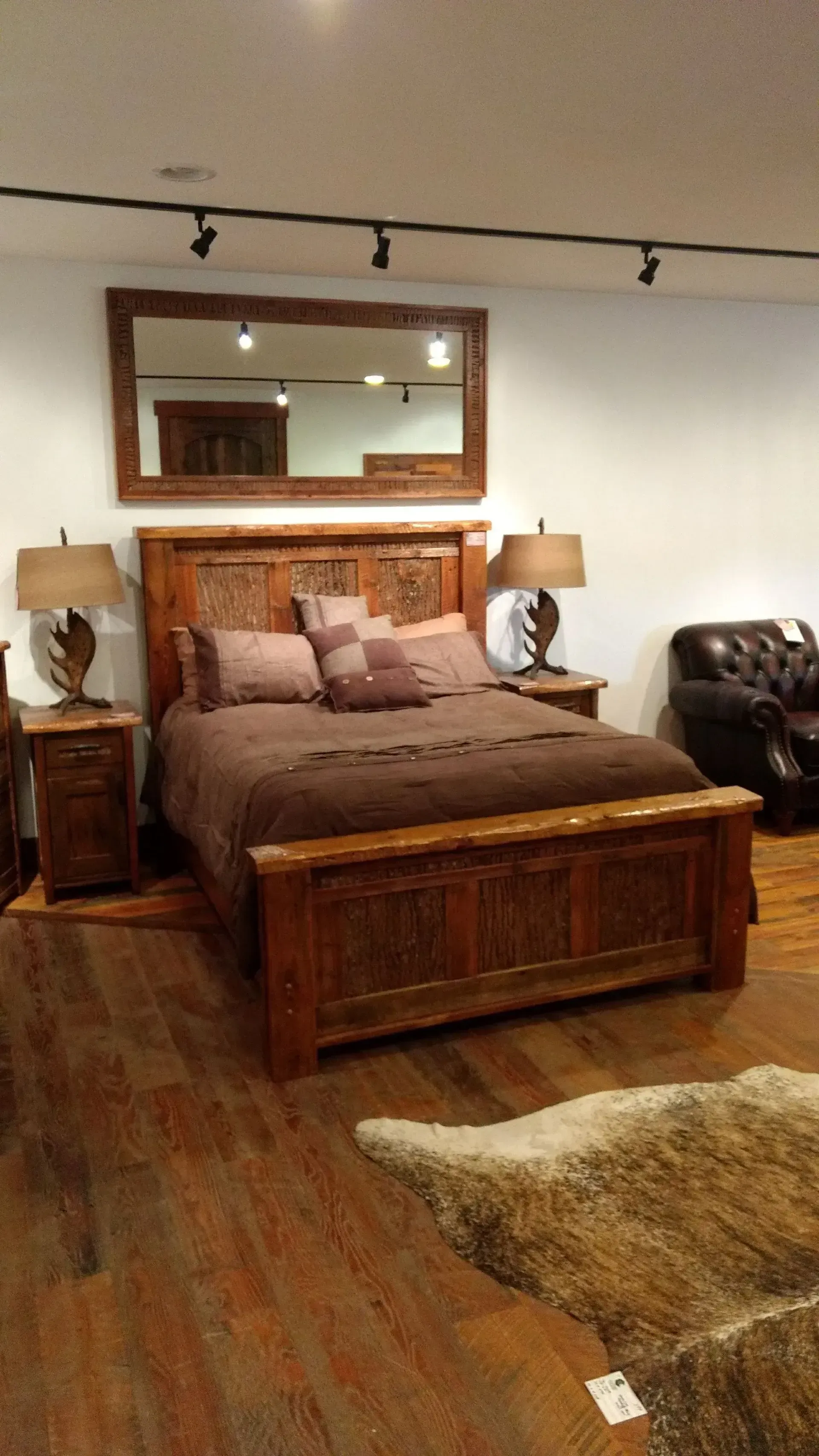 Rustic bedroom with wooden bed frame, brown bedding, nightstands, mirror, and fur rug