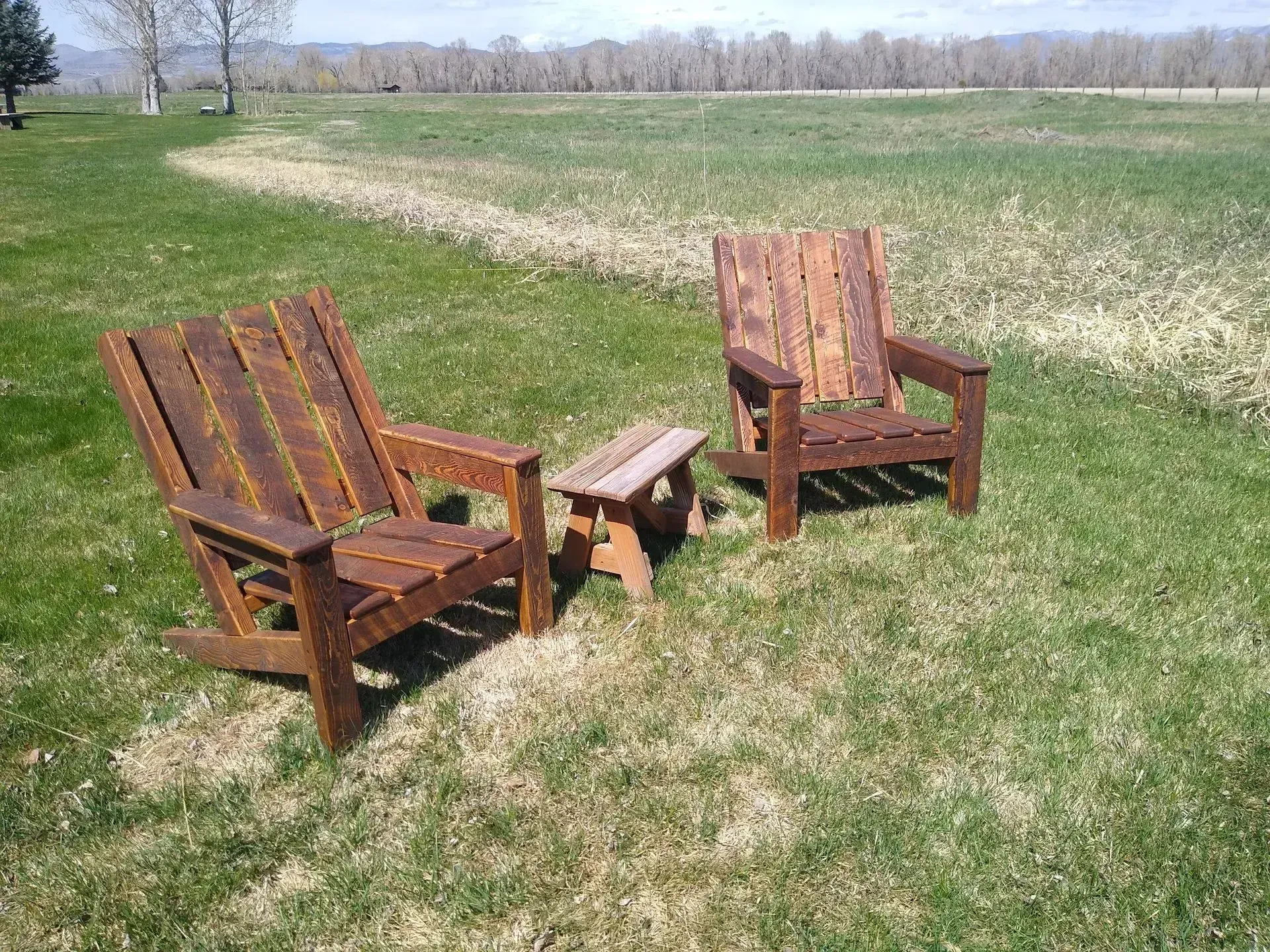 Two wooden chairs with a small table on grass in a sunny field
