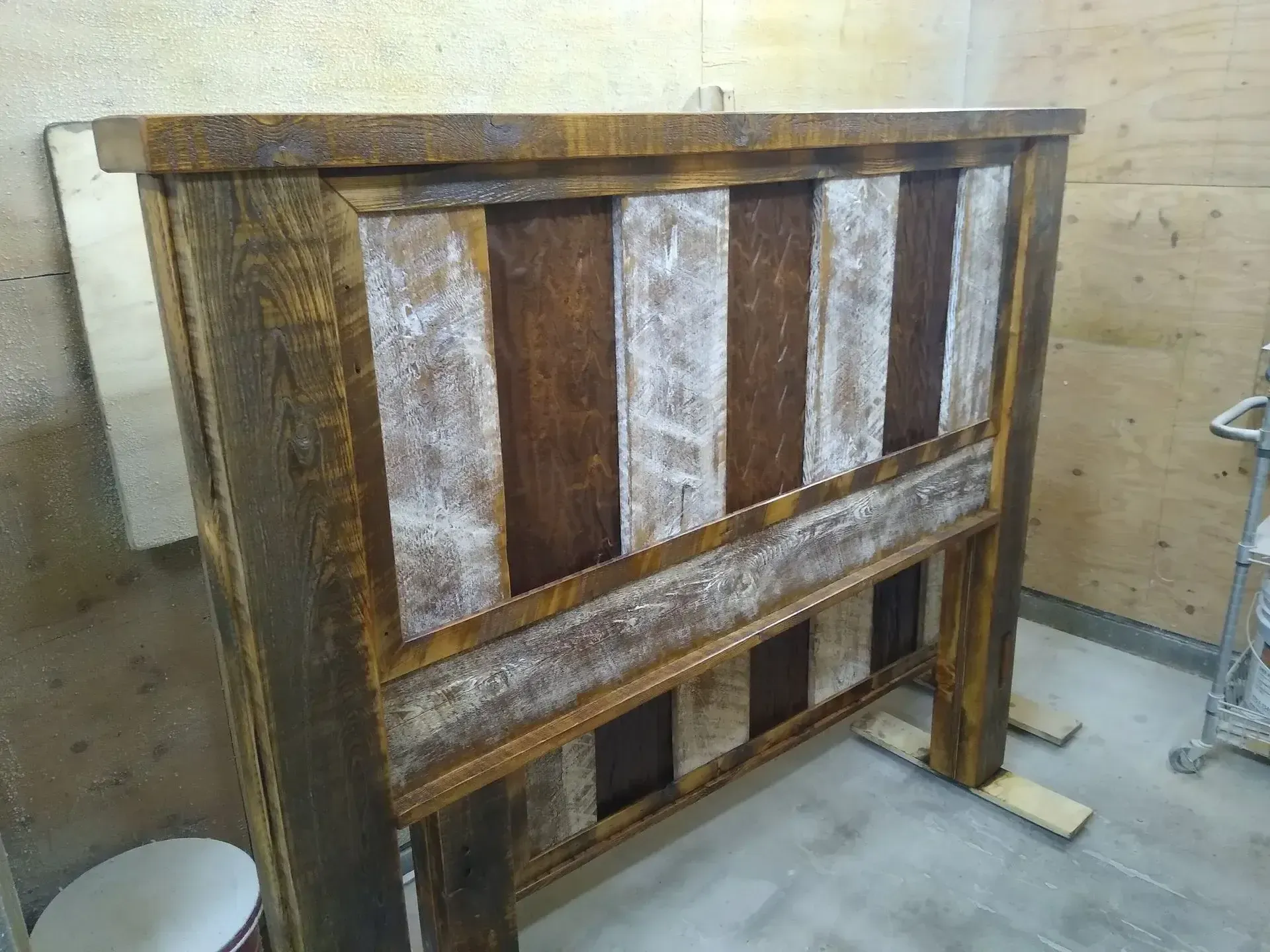 Wooden headboard or panel with vertical slats, leaning against a workshop wall.