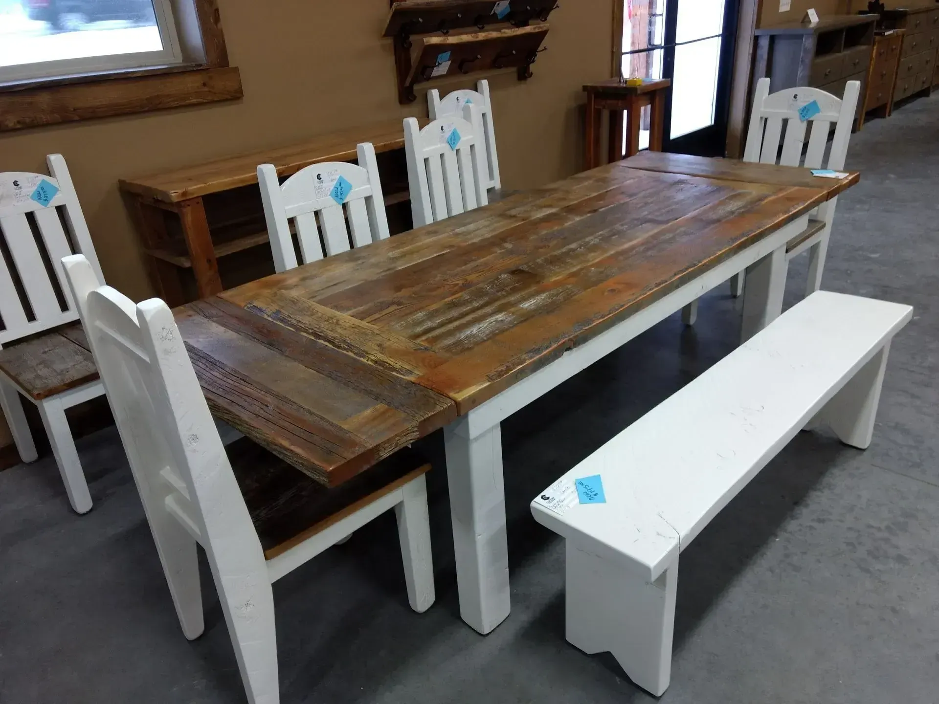 Rustic wooden dining table with white chairs and benches in a room with gray carpet