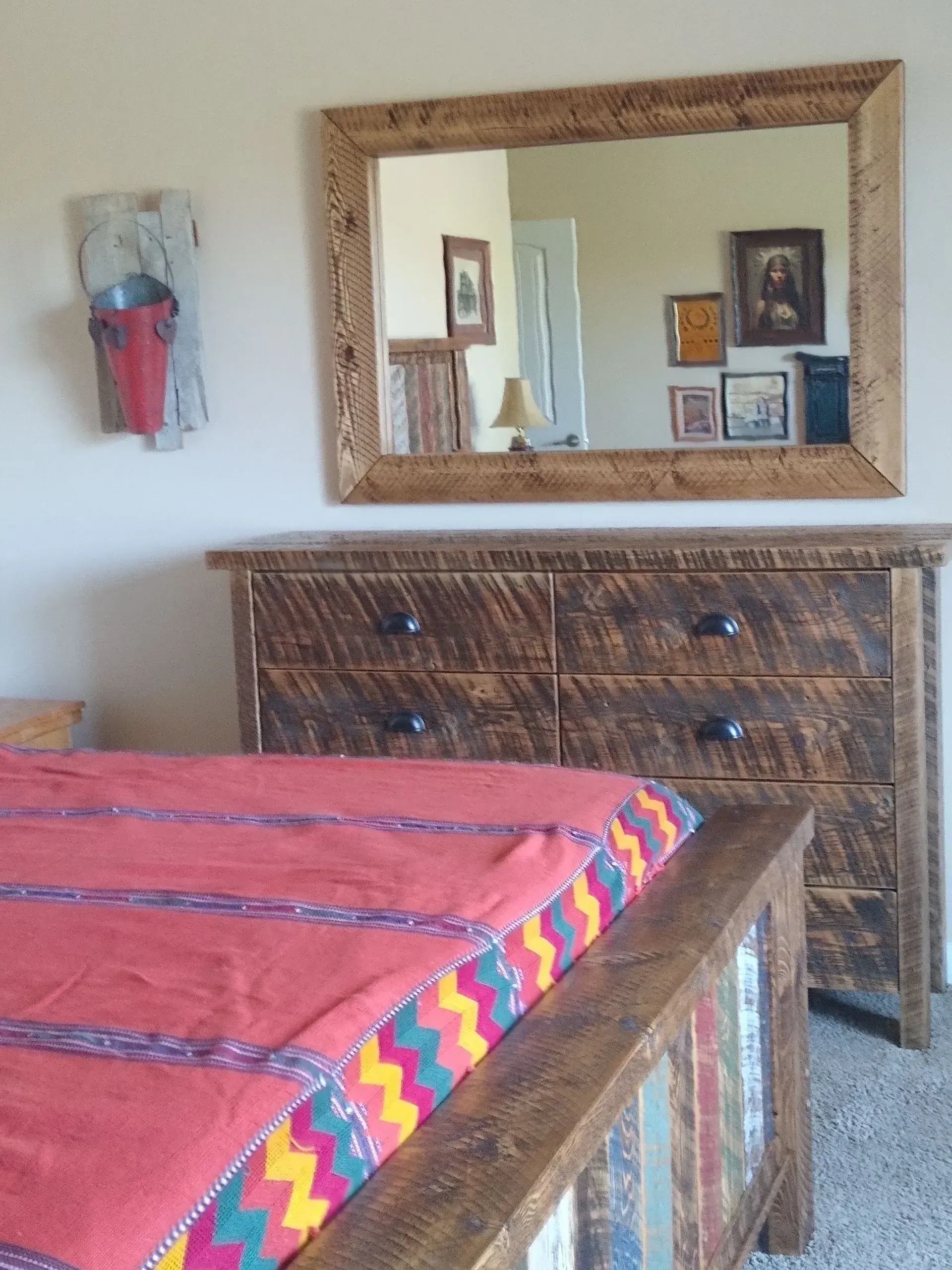 Bedroom with red bedspread, wooden dresser, and large wall mirror reflecting the room.