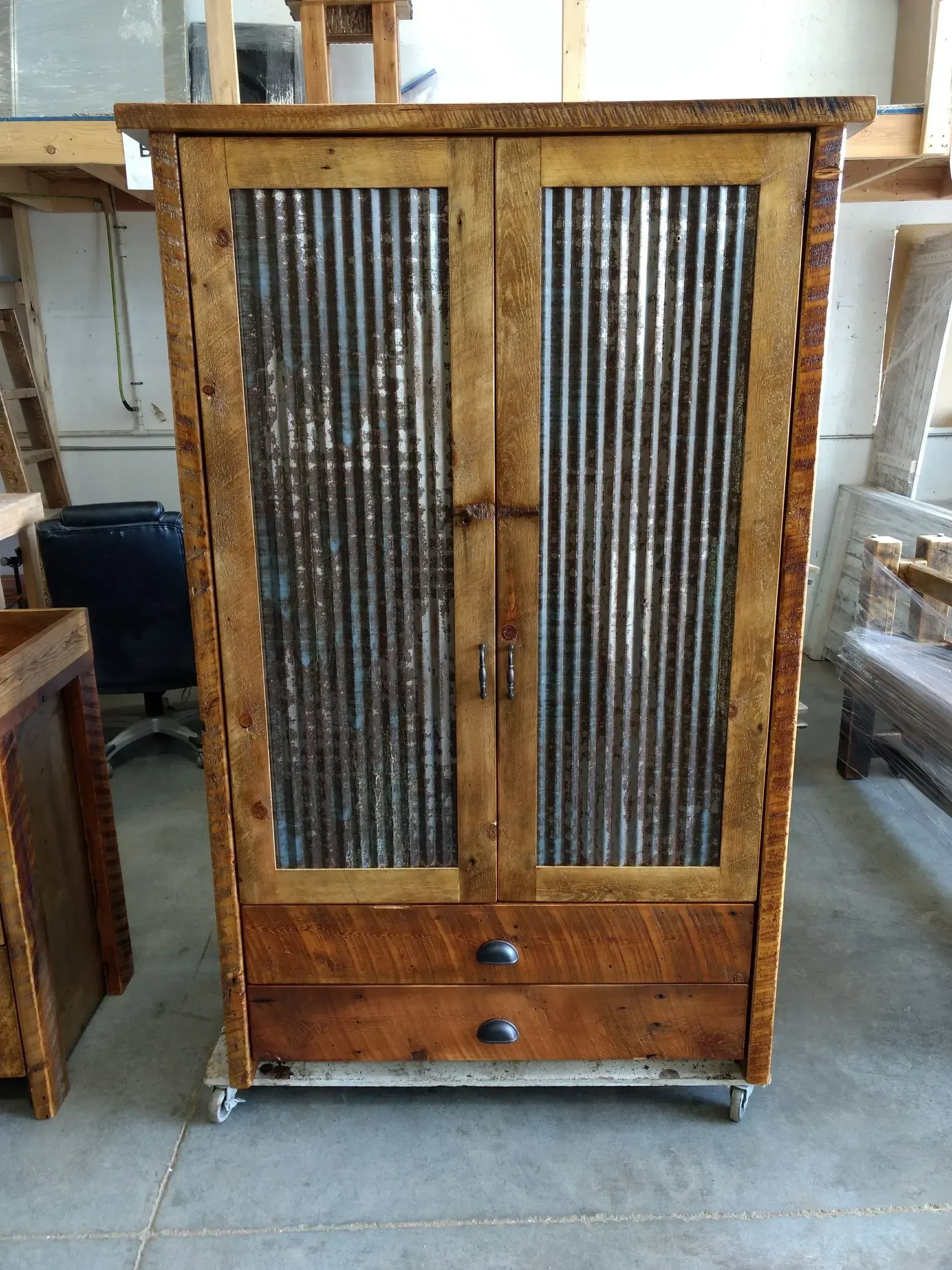 Wooden cabinet with two corrugated metal doors and a drawer, standing in a workshop.
