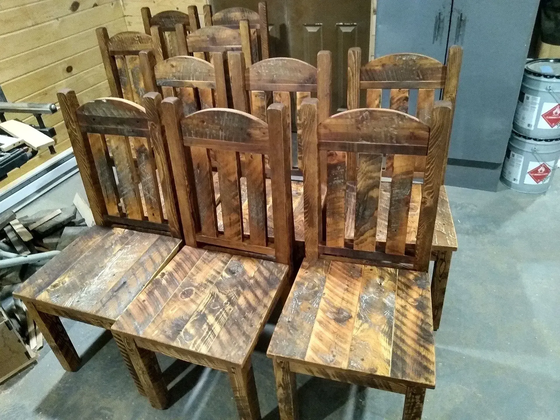 Stack of rustic wooden chairs with slatted backs in a workshop or storage area