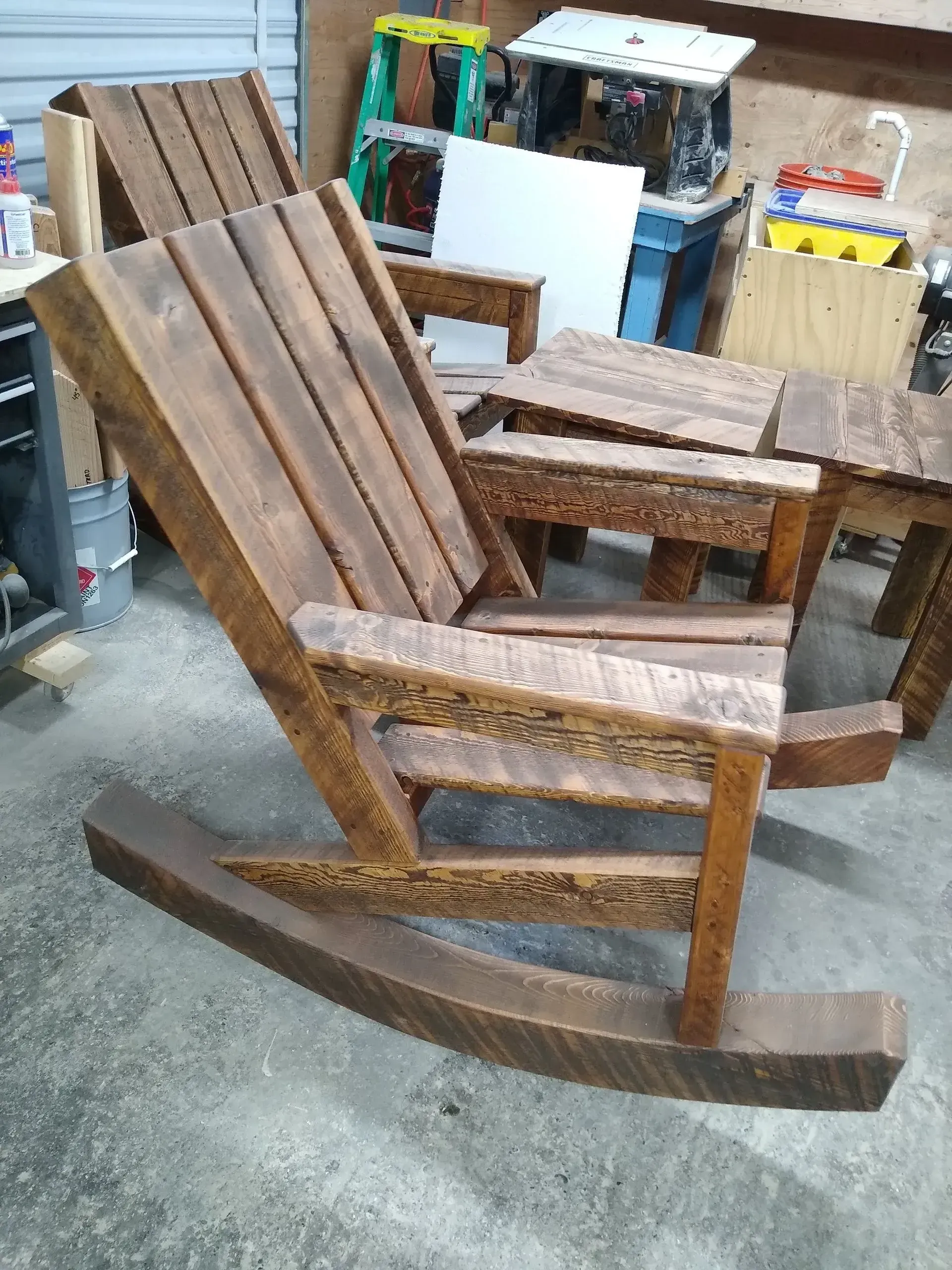 Wooden rocking chairs in a workshop, with one chair in the foreground and others behind it.