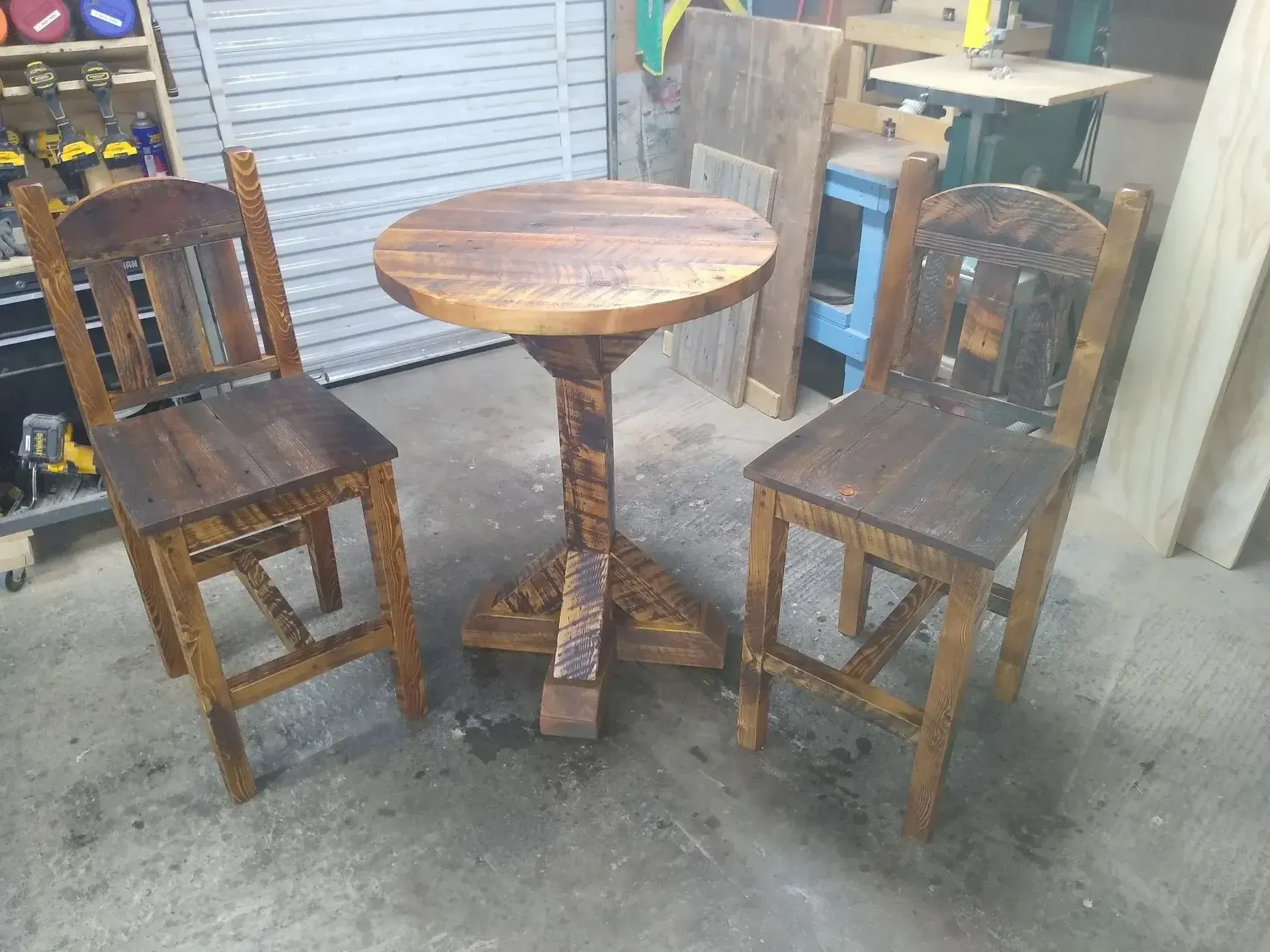 Small round wooden table with two wooden chairs in a workshop or garage setting