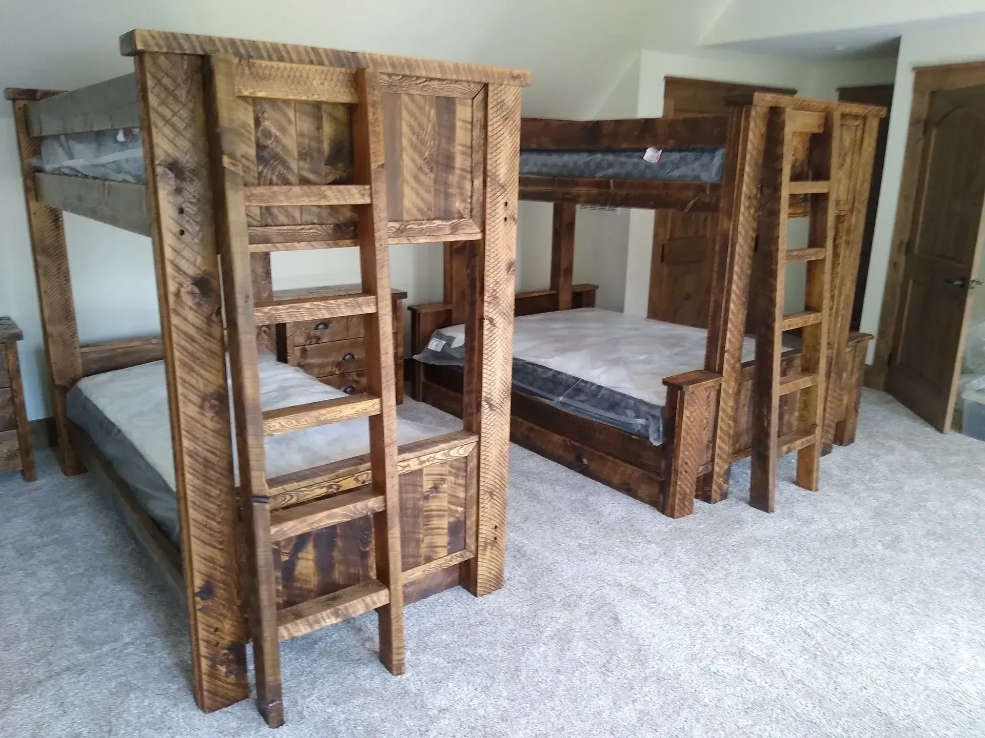 Three rustic wooden bunk beds in a carpeted bedroom with white walls