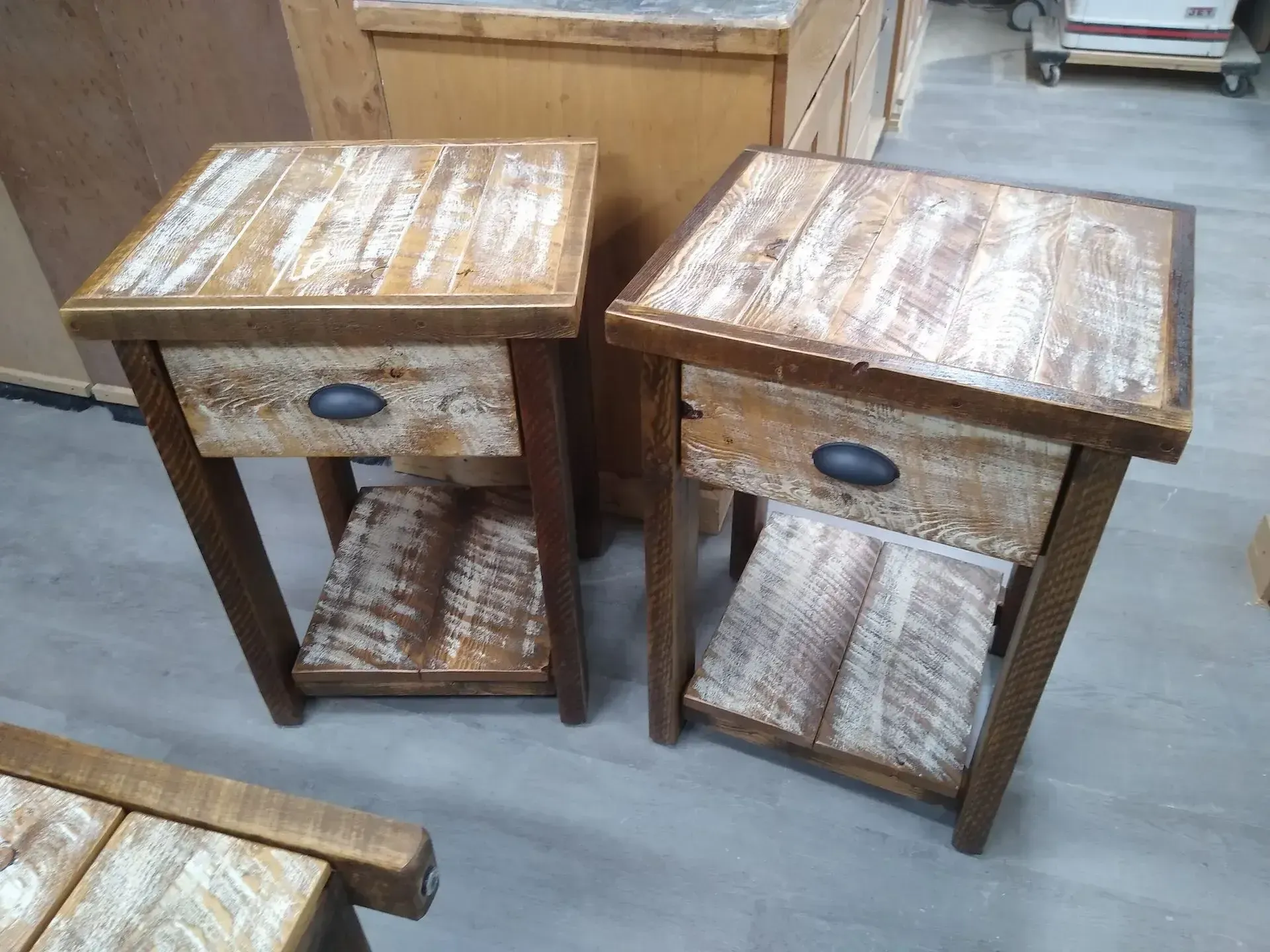 Two rustic wooden bedside tables with drawers and lower shelves on a concrete floor