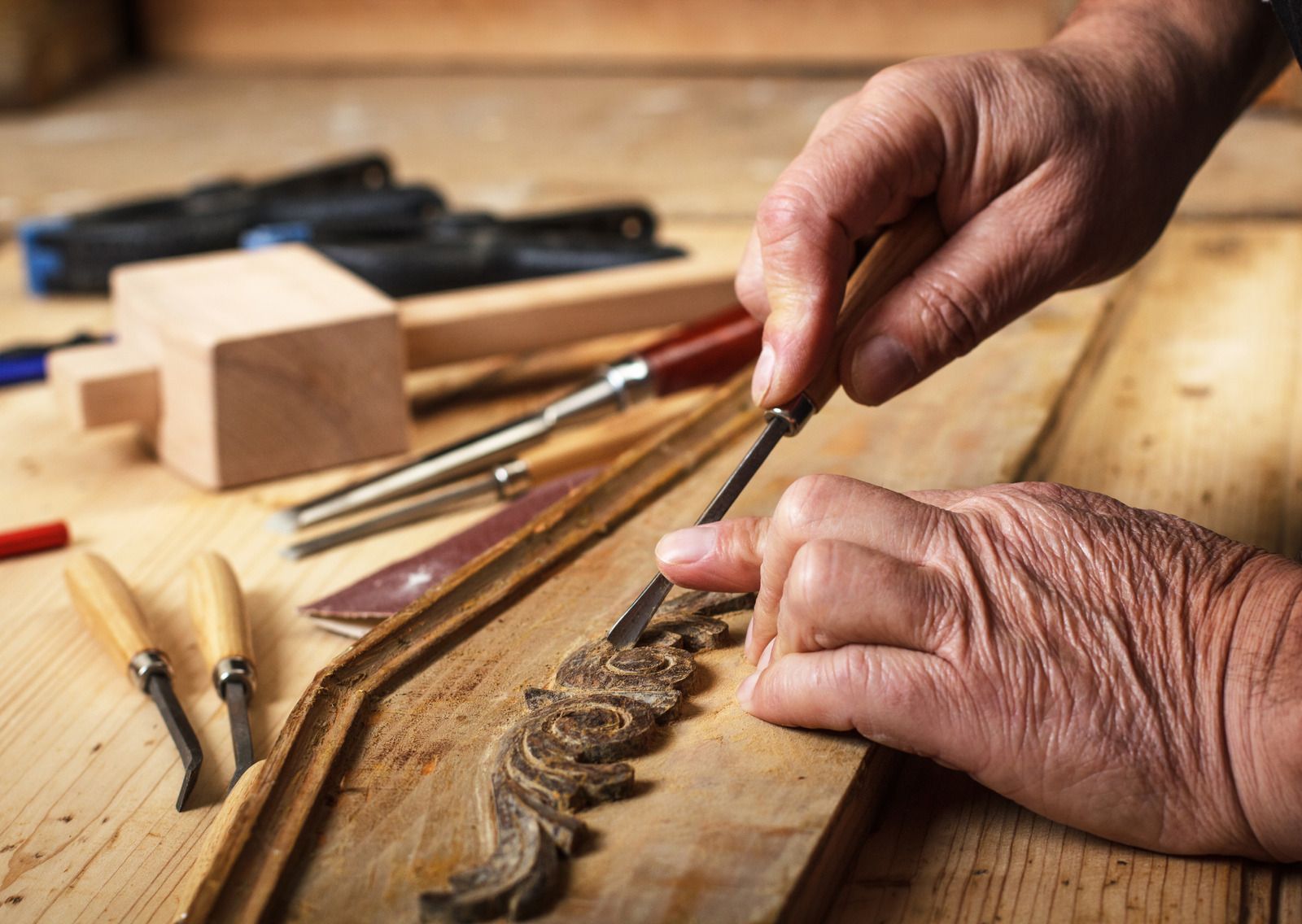 Hands carving wood with chisels on a workbench in a workshop