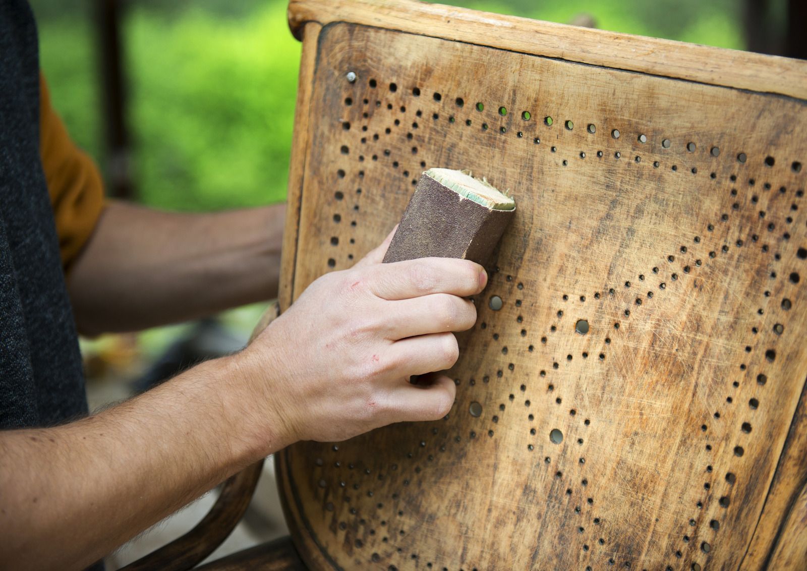 Hand sanding a perforated wooden chair back outdoors