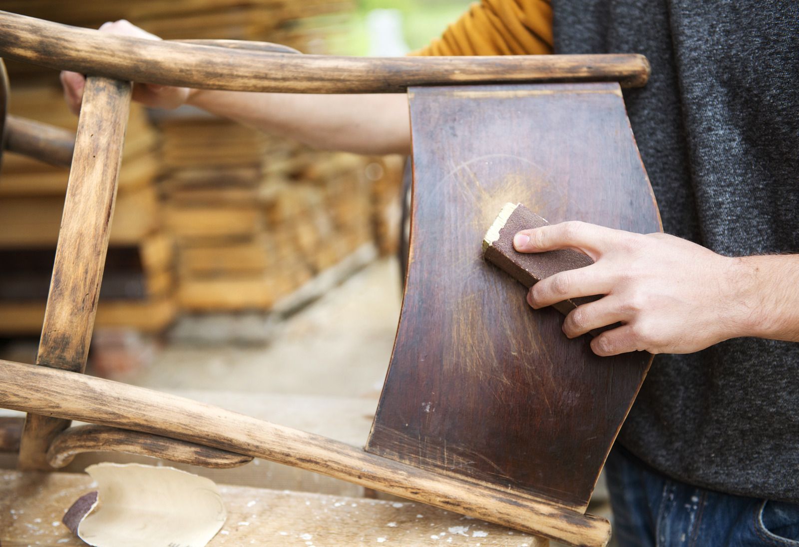 Hand sanding a dark wooden board on a rustic wooden structure outdoors