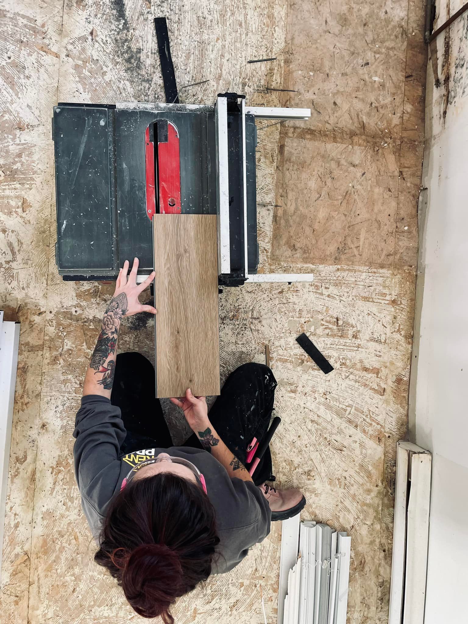 Person installing wood flooring in a room under renovation.