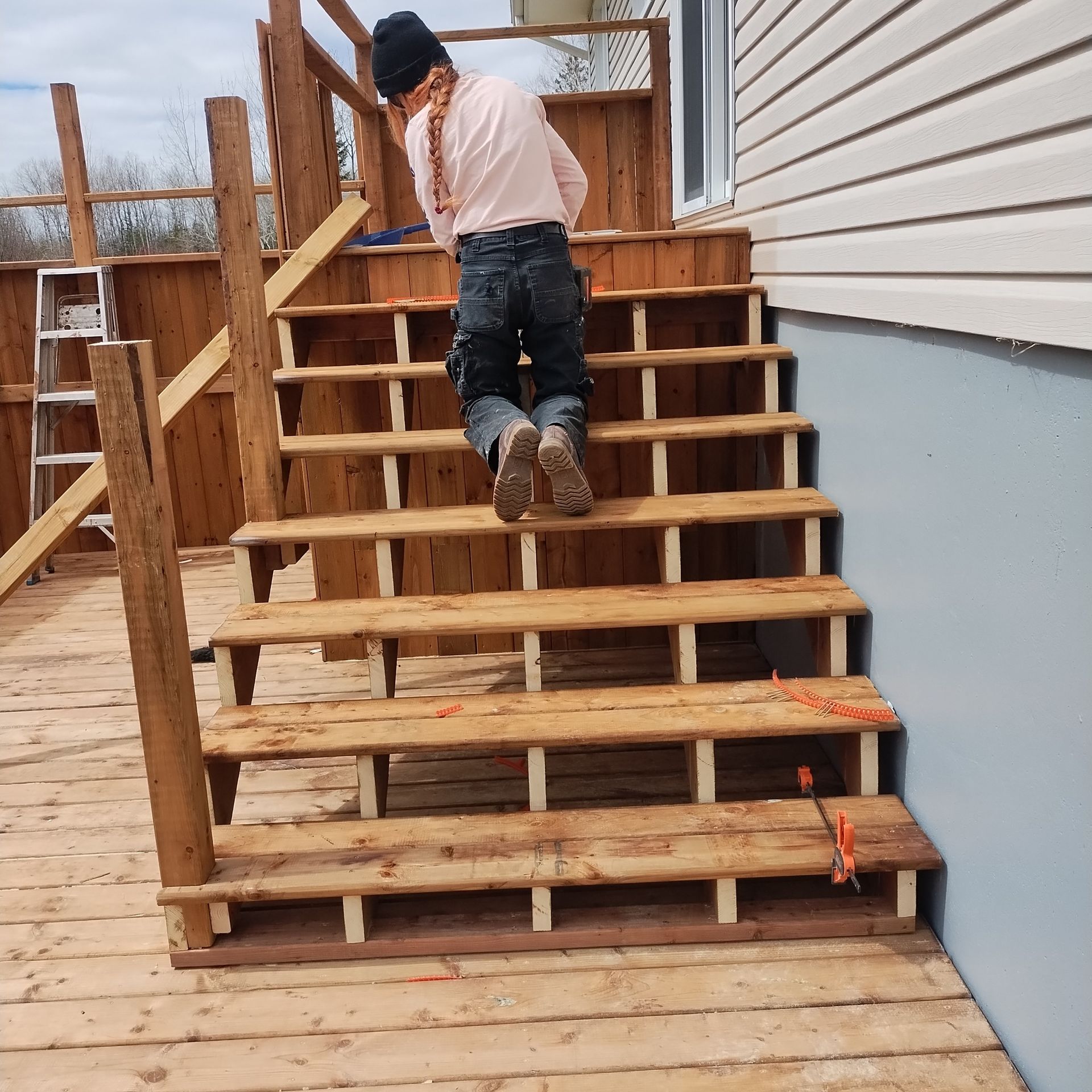 A person building a wooden staircase on a deck, with partially assembled steps and gold markings.