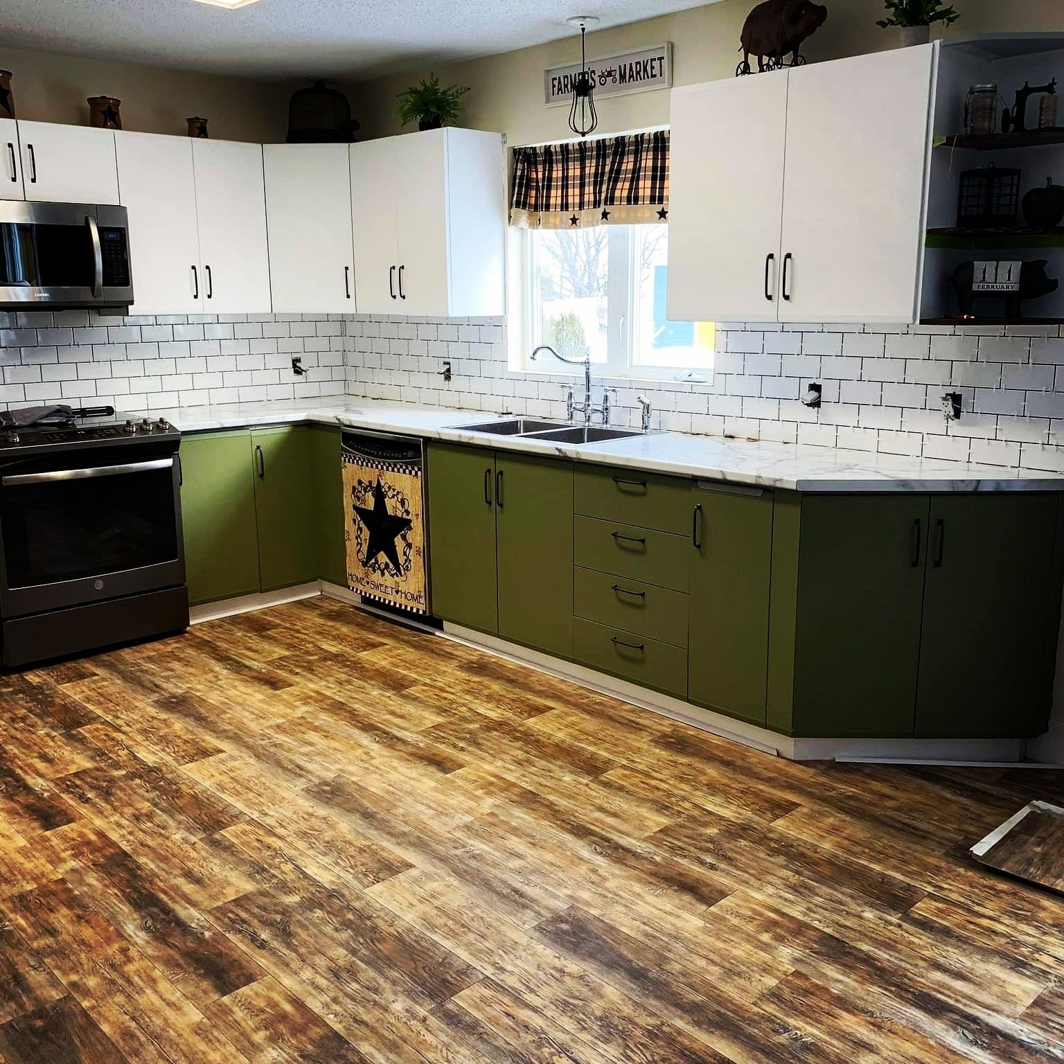 Kitchen with white and green cabinets, white countertops, white subway tile backsplash and wood flooring.