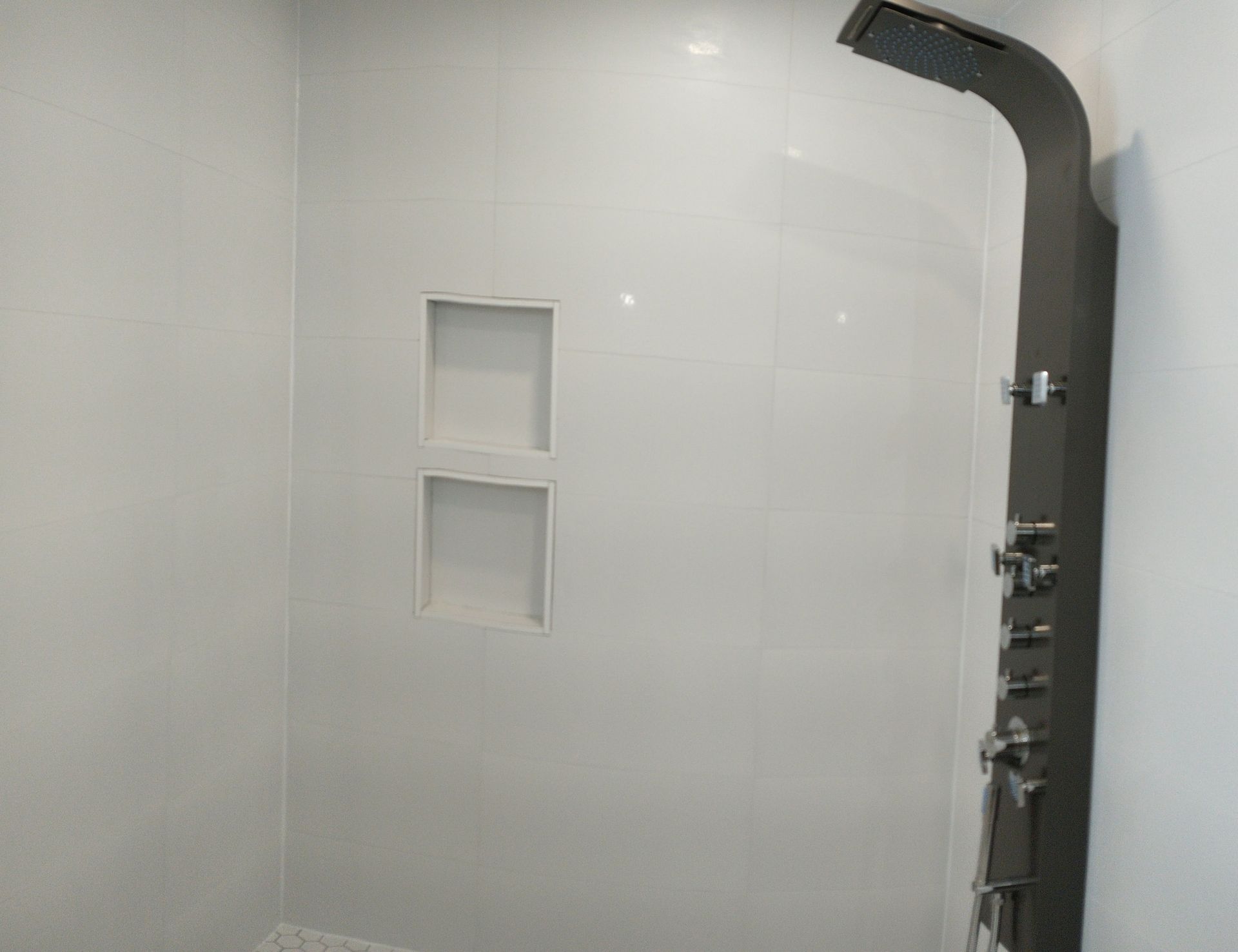 Shower room with white tile, wall niches and black shower column.