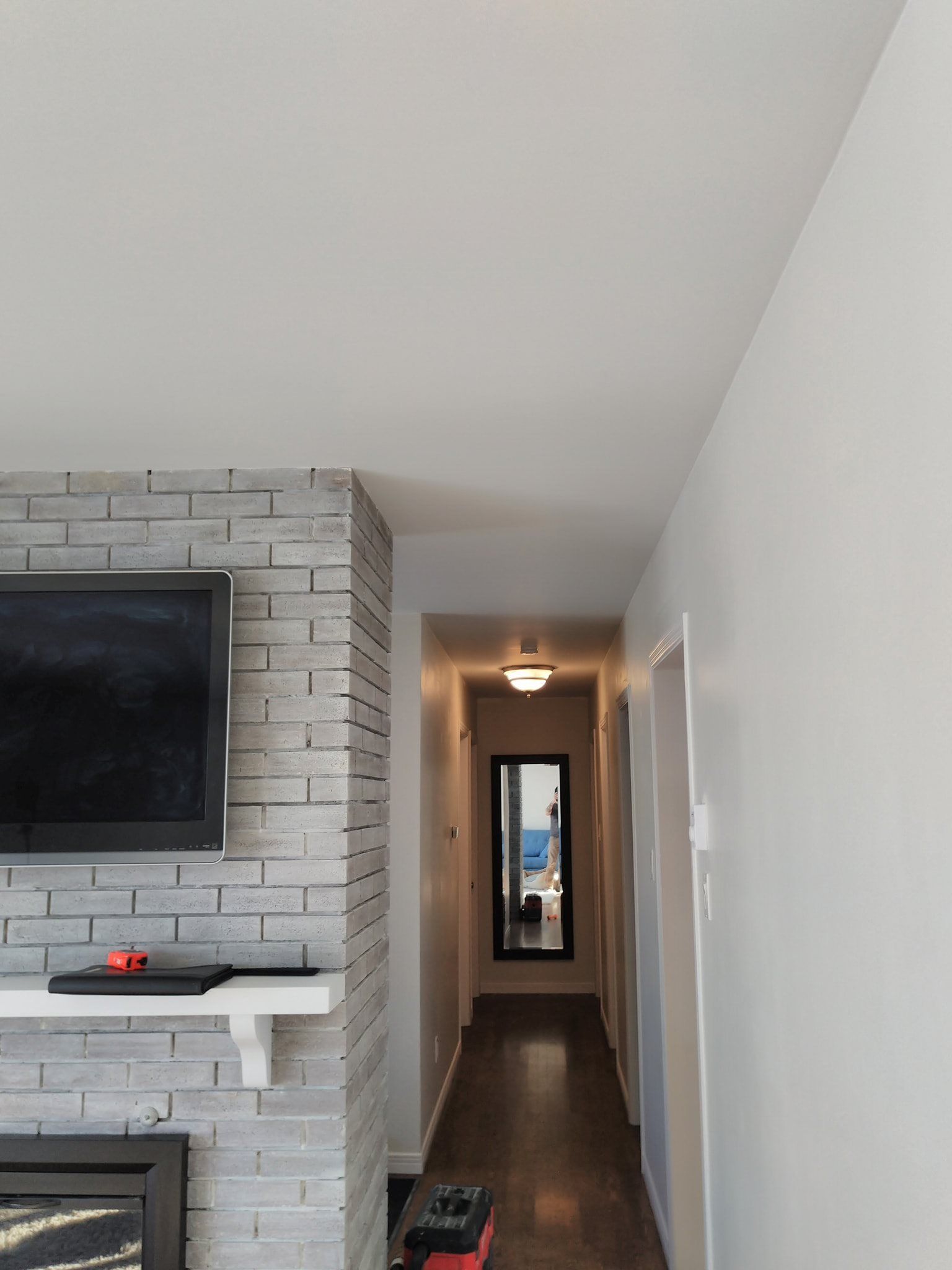 Hallway with white walls, fireplace with wall-mounted TV and gray brick.