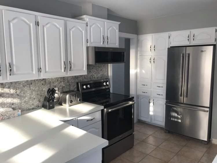Renovated kitchen with white cabinets, stainless steel appliances and white countertop.