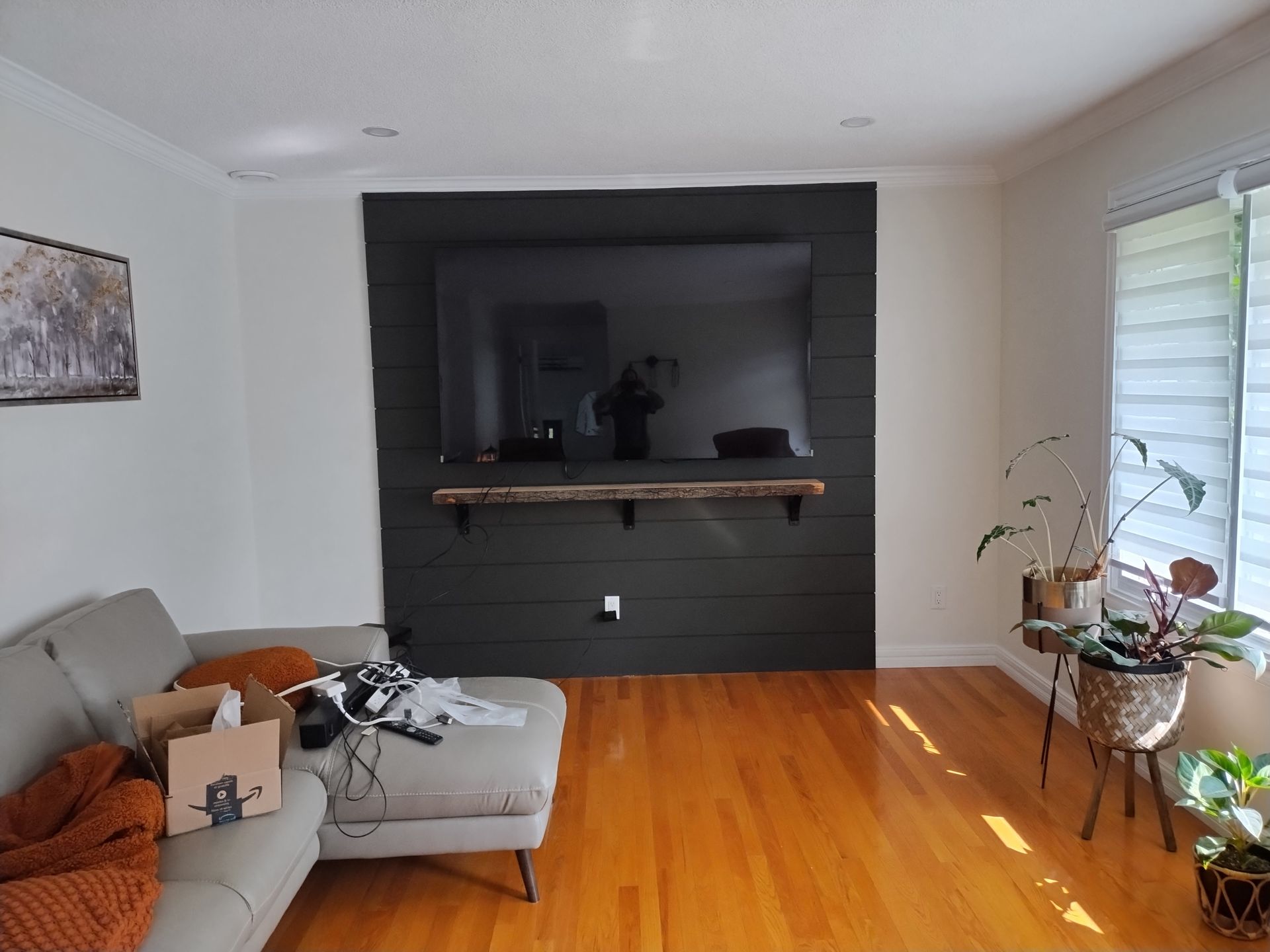 Living room with wall-mounted TV on black background, wood shelving, white sofa and indoor plants.