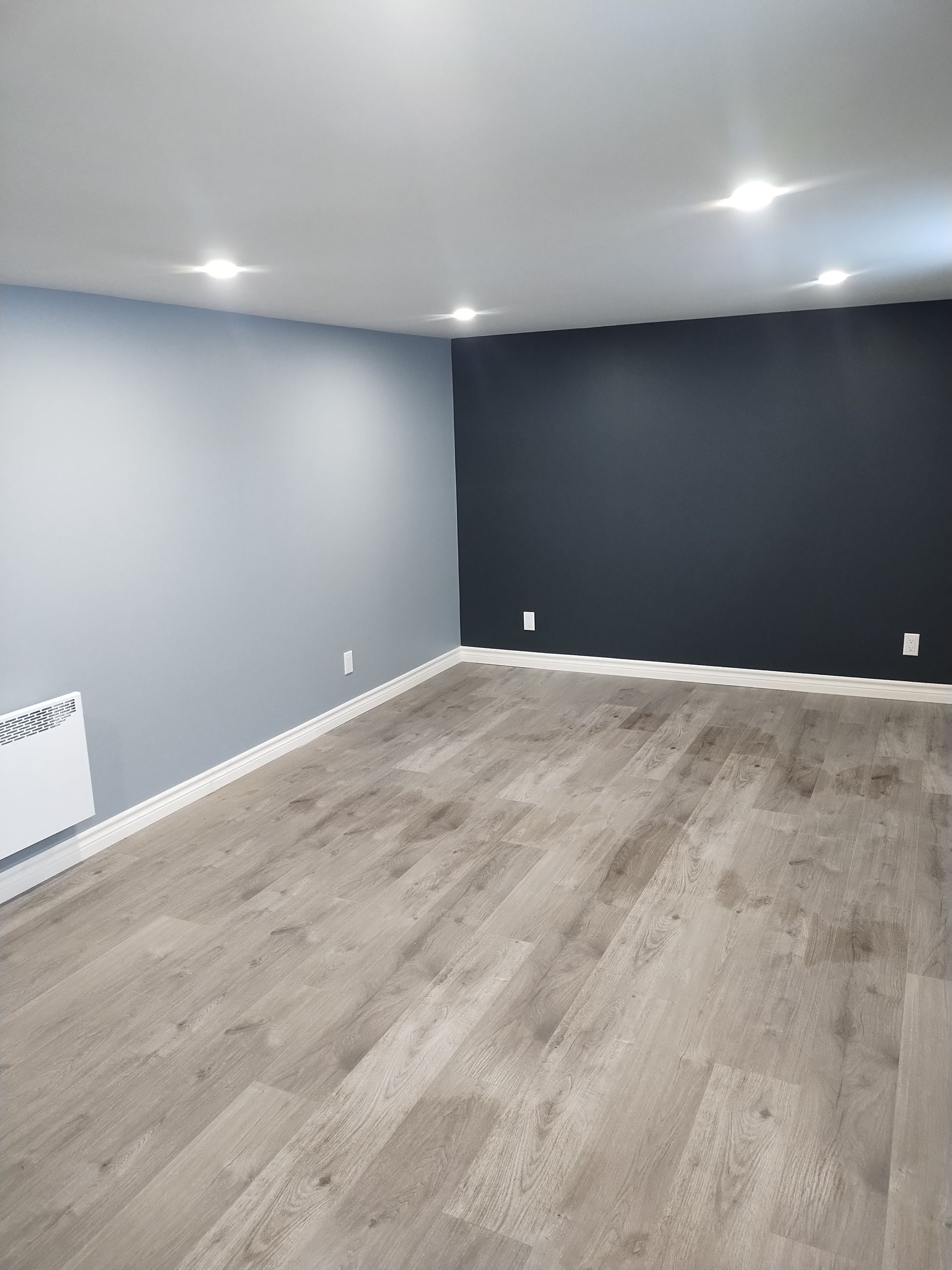 Empty room with blue and black painted walls, laminate flooring and recessed lighting.