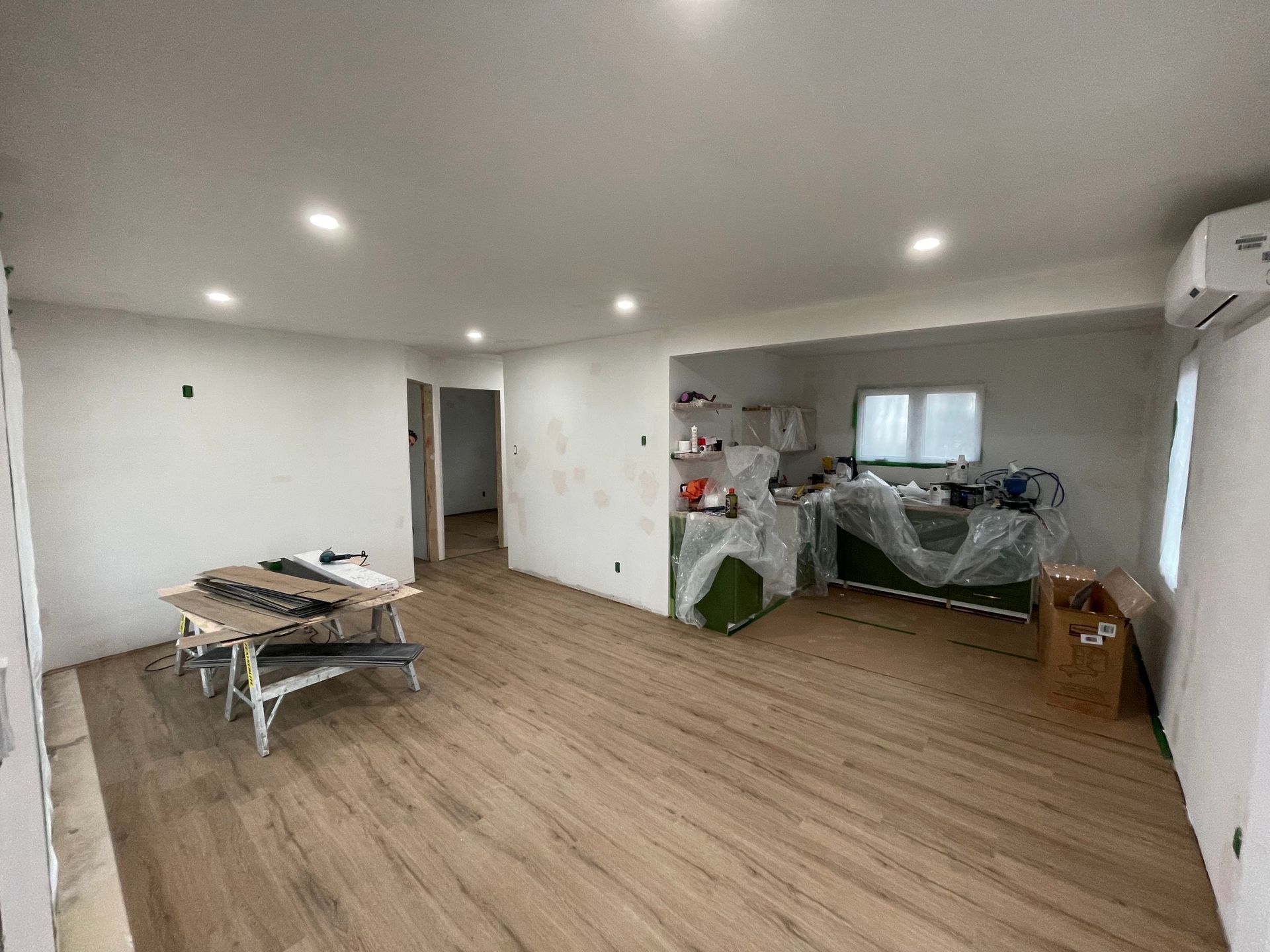 Empty room with wood flooring, white walls and appliances covered in plastic.
