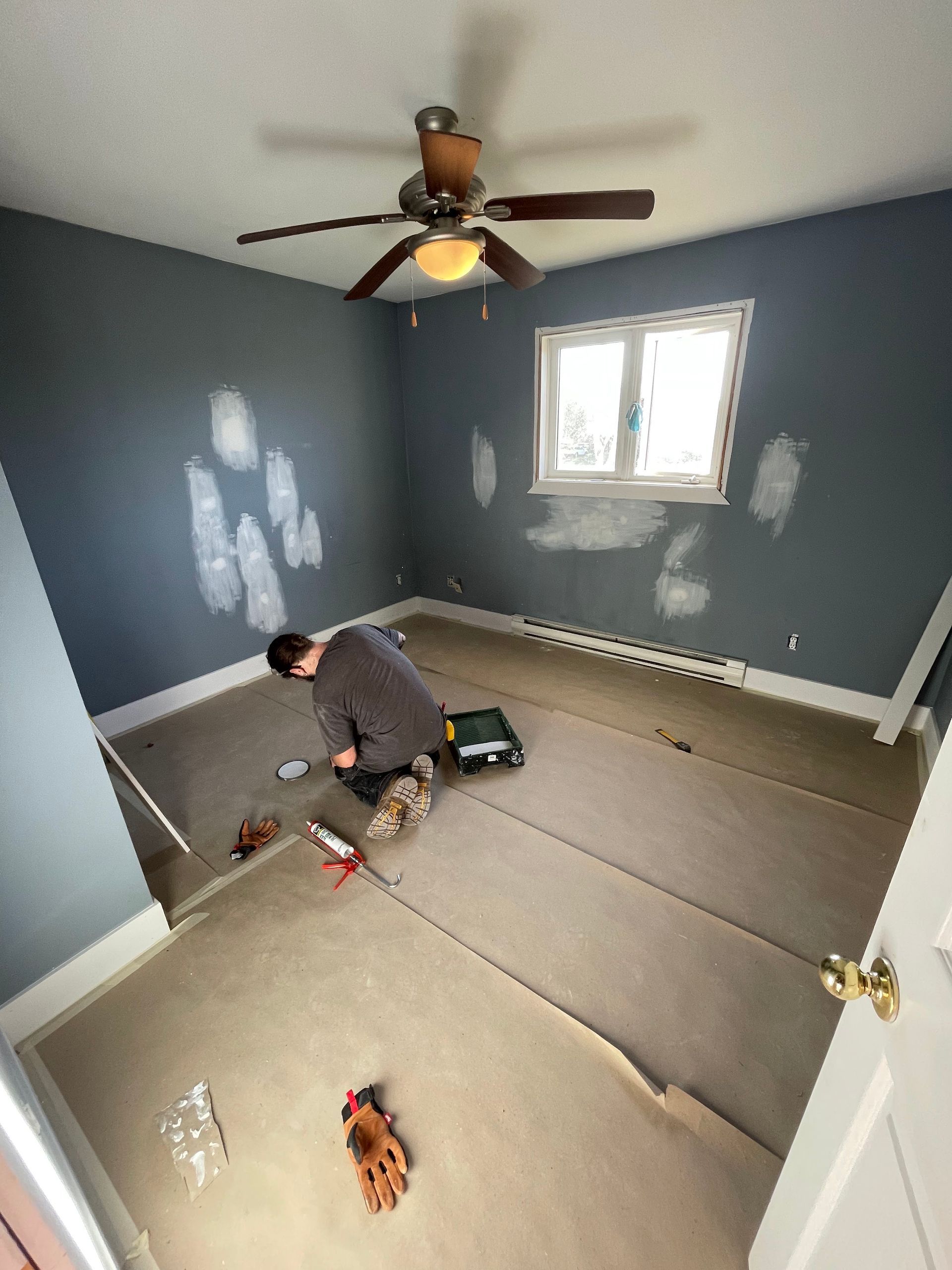 Worker performing wall repairs in a room with gray paint.