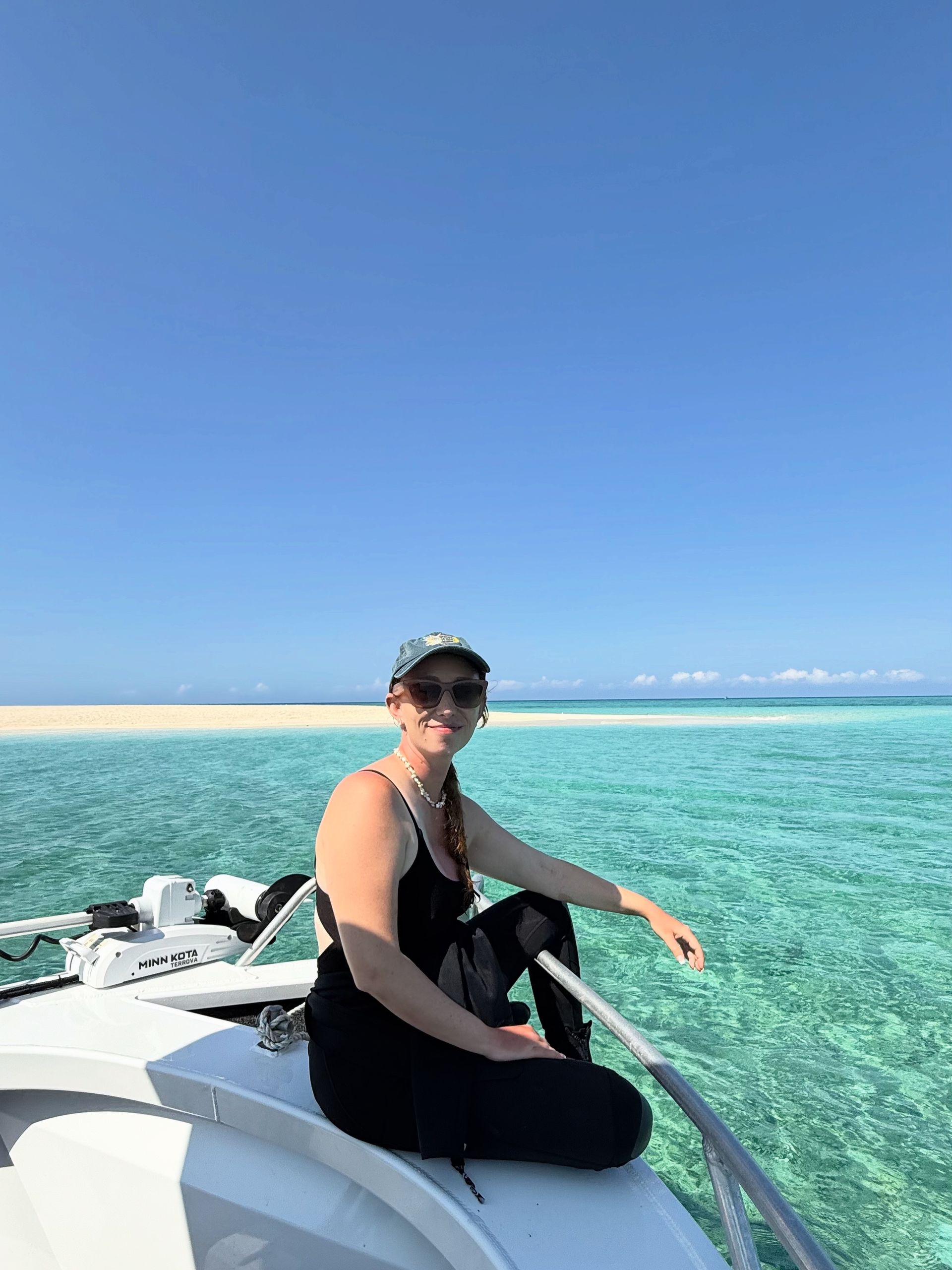 Jacinta sitting on a boat in dive gear with turquoise water under a clear blue sky on the Great Barrier Reef