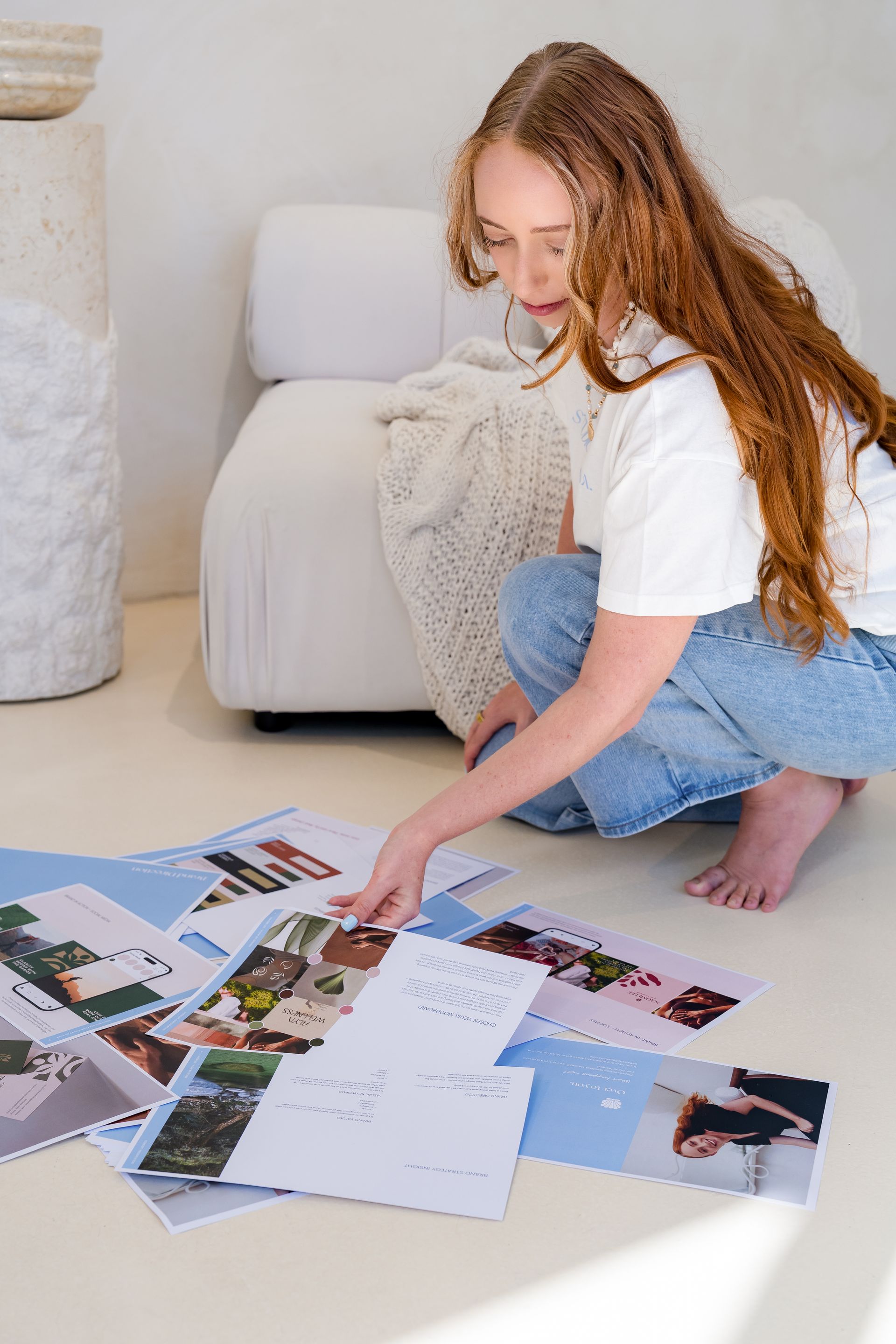 Woman kneeling on a floor, arranging scattered brand identity design brand guidelines while planning in a bright room