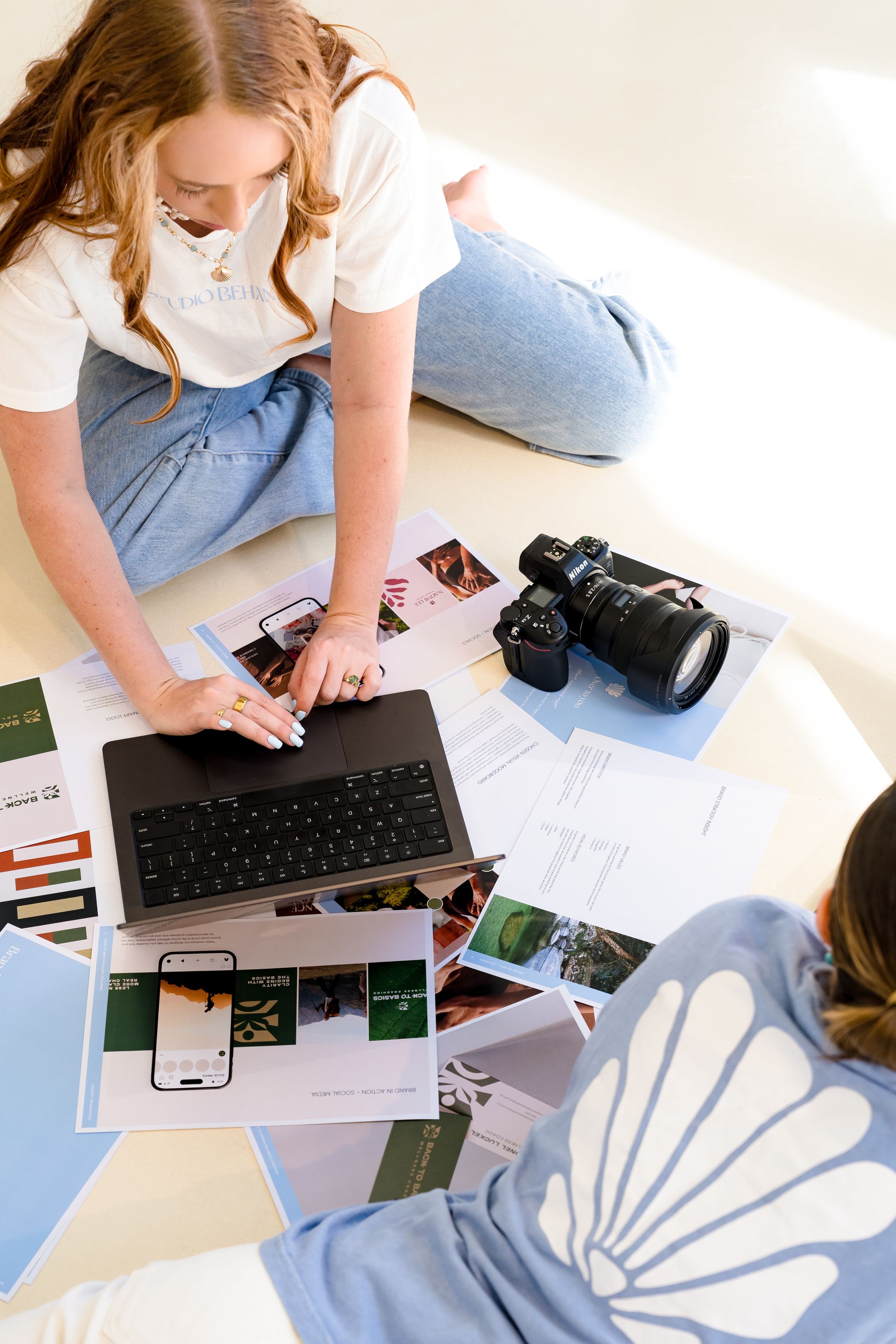 Jacinta, founder of Studio Behana using a laptop on the floor beside a camera and printed brand identity design pages.