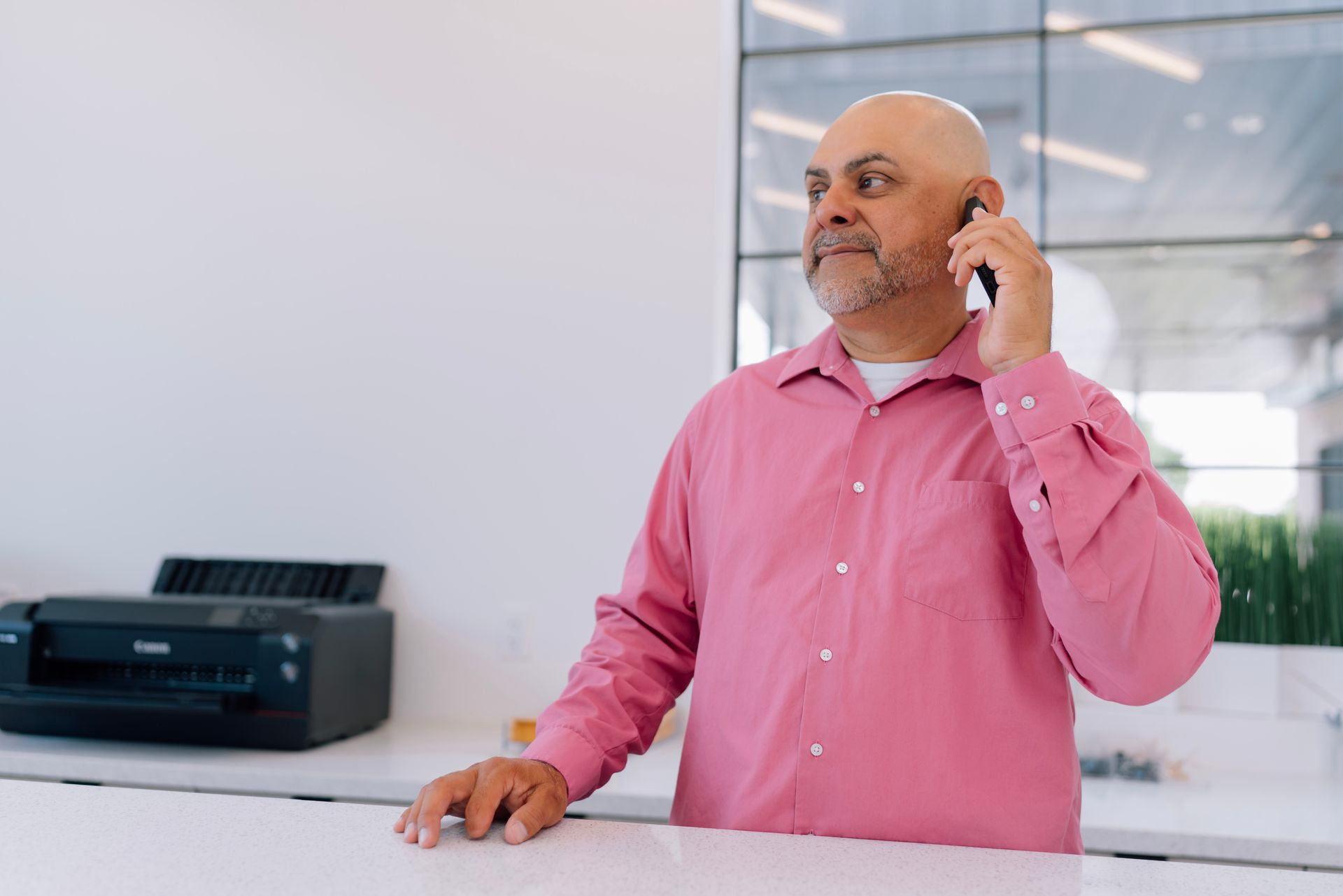 A man in a pink shirt is talking on a cell phone.